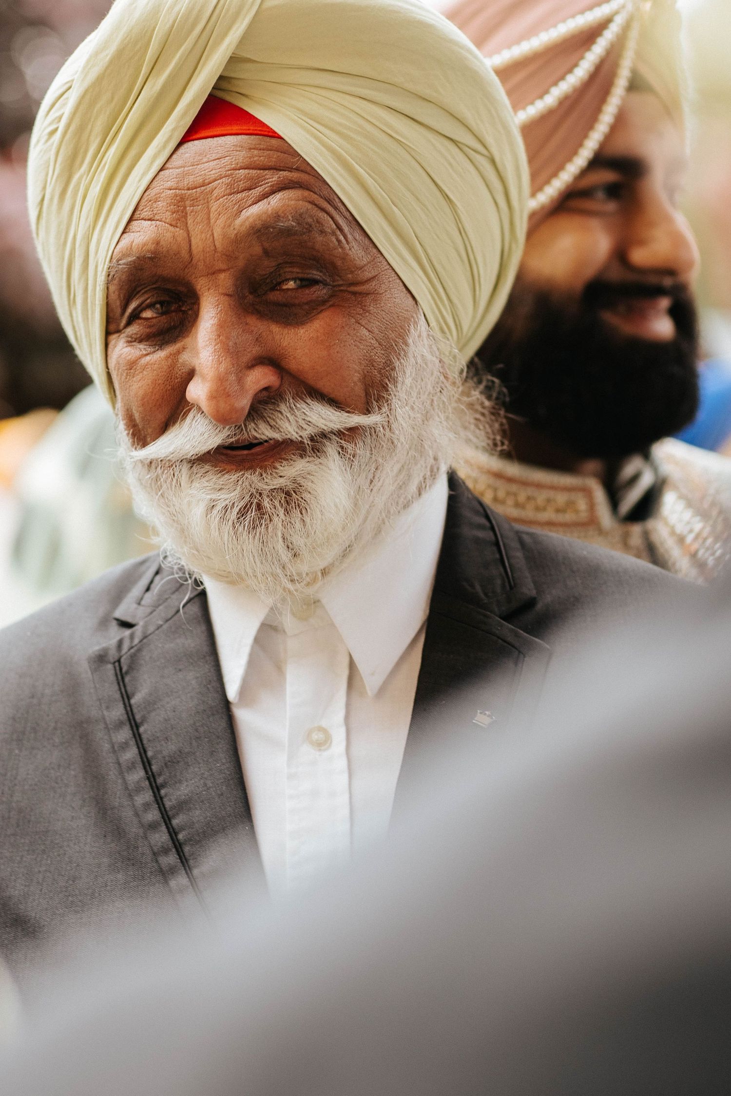 Close-up views of an elderly Sikh gentleman wearing a white turban and gray suit against a blurred background.