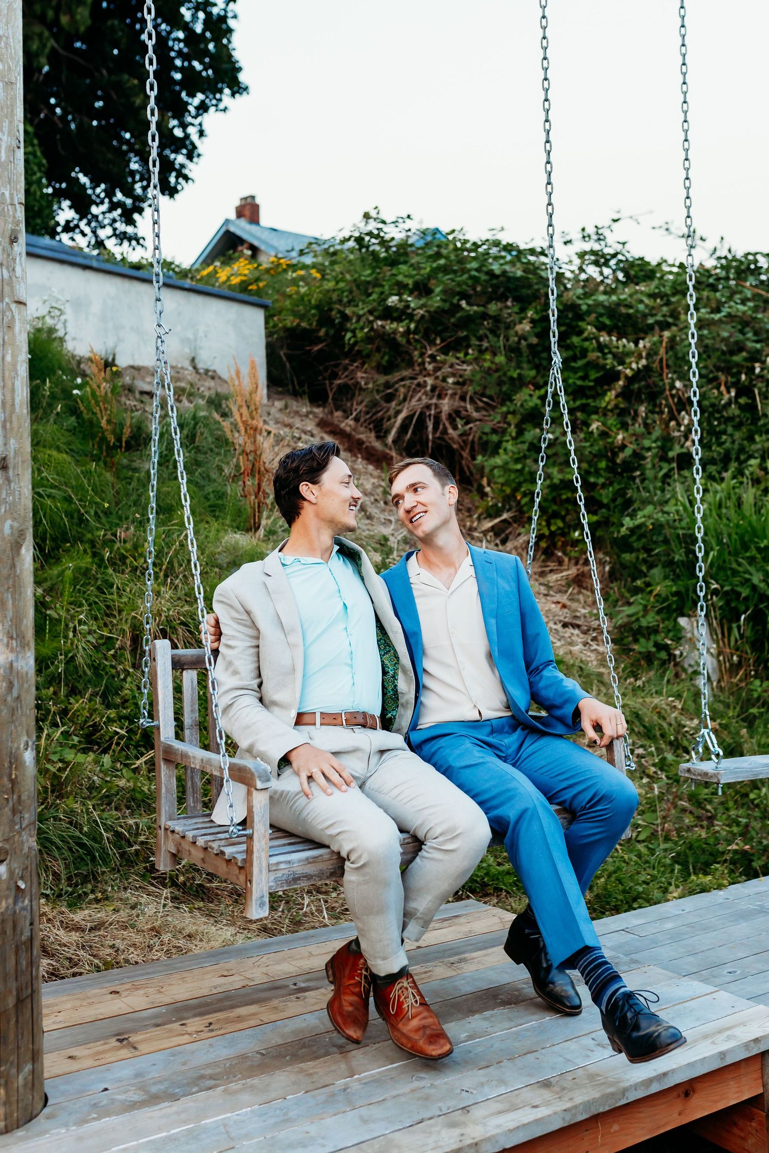Two people sharing a tender moment while sitting together on a wooden deck swing in a garden setting.