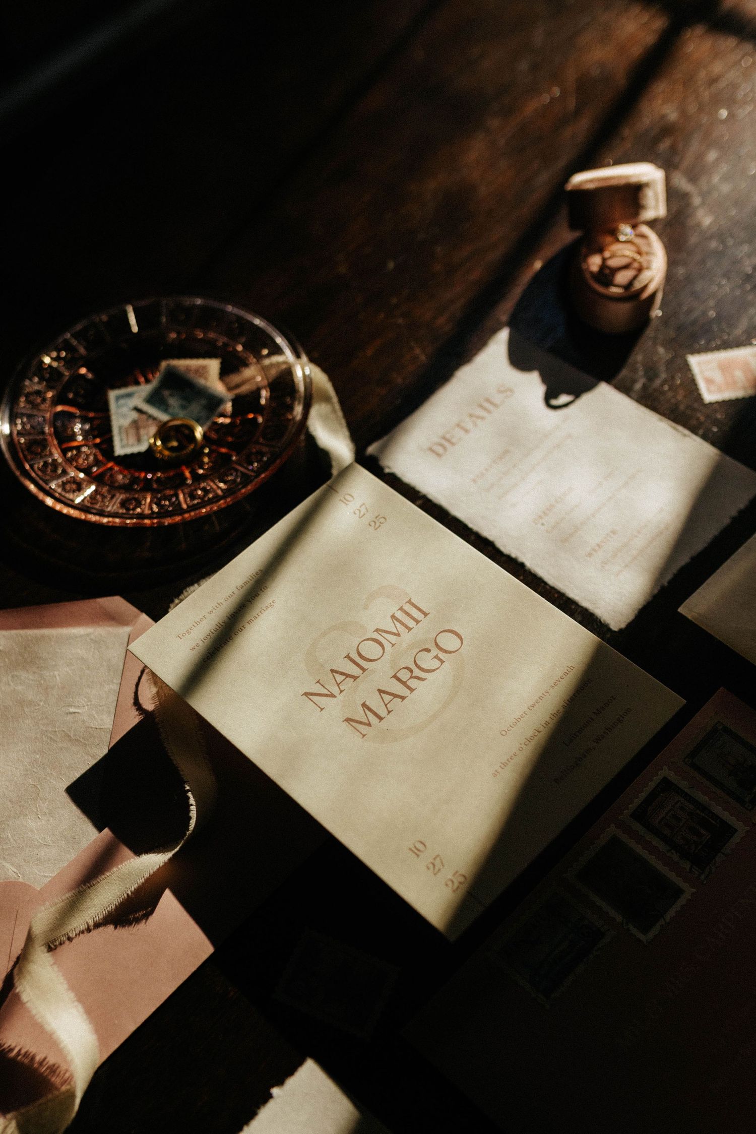 Wedding stationery flatlay featuring personalized book, ring box, and details card in moody lighting.
