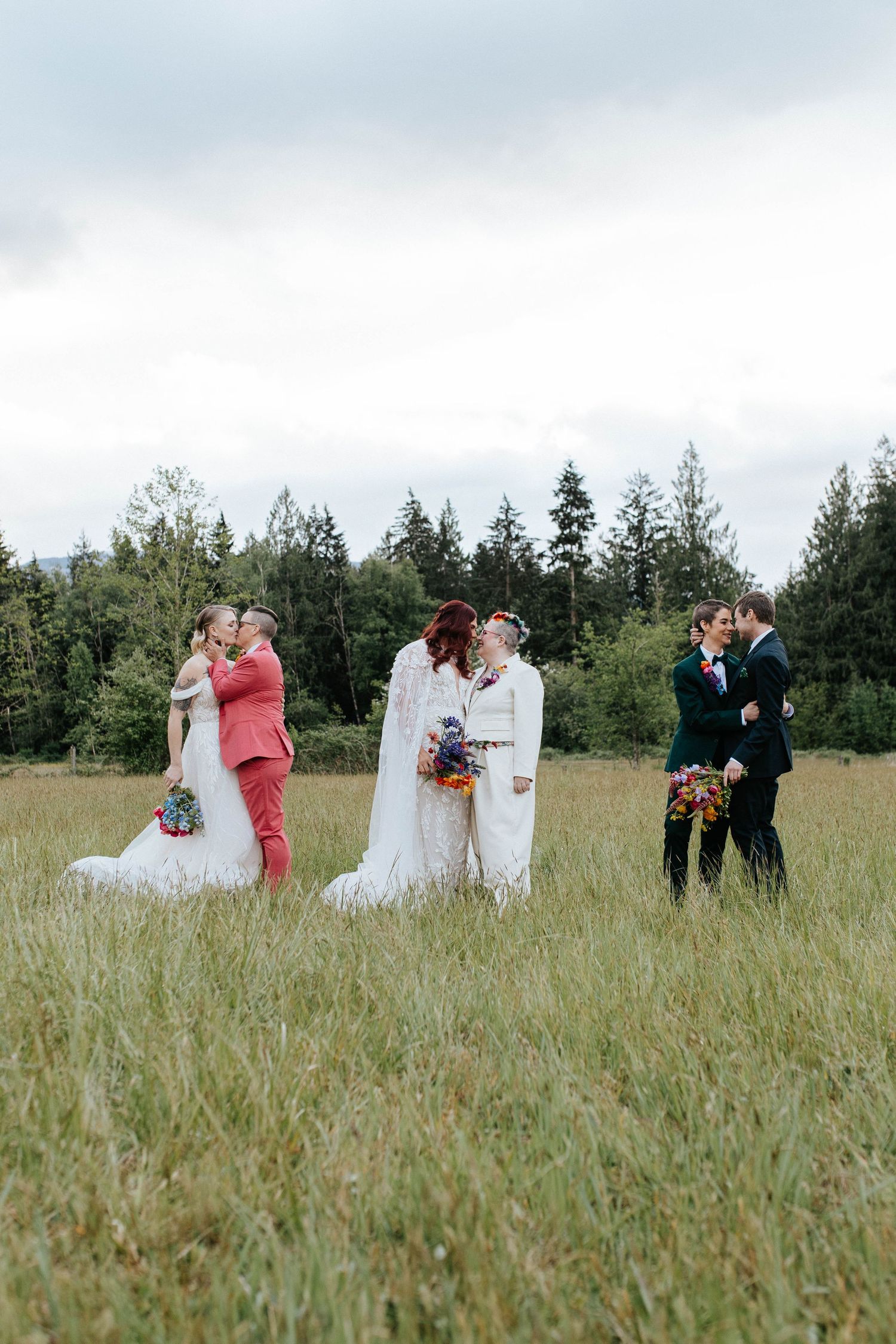 Wedding party stands in field of tall grass with evergreen trees in background.