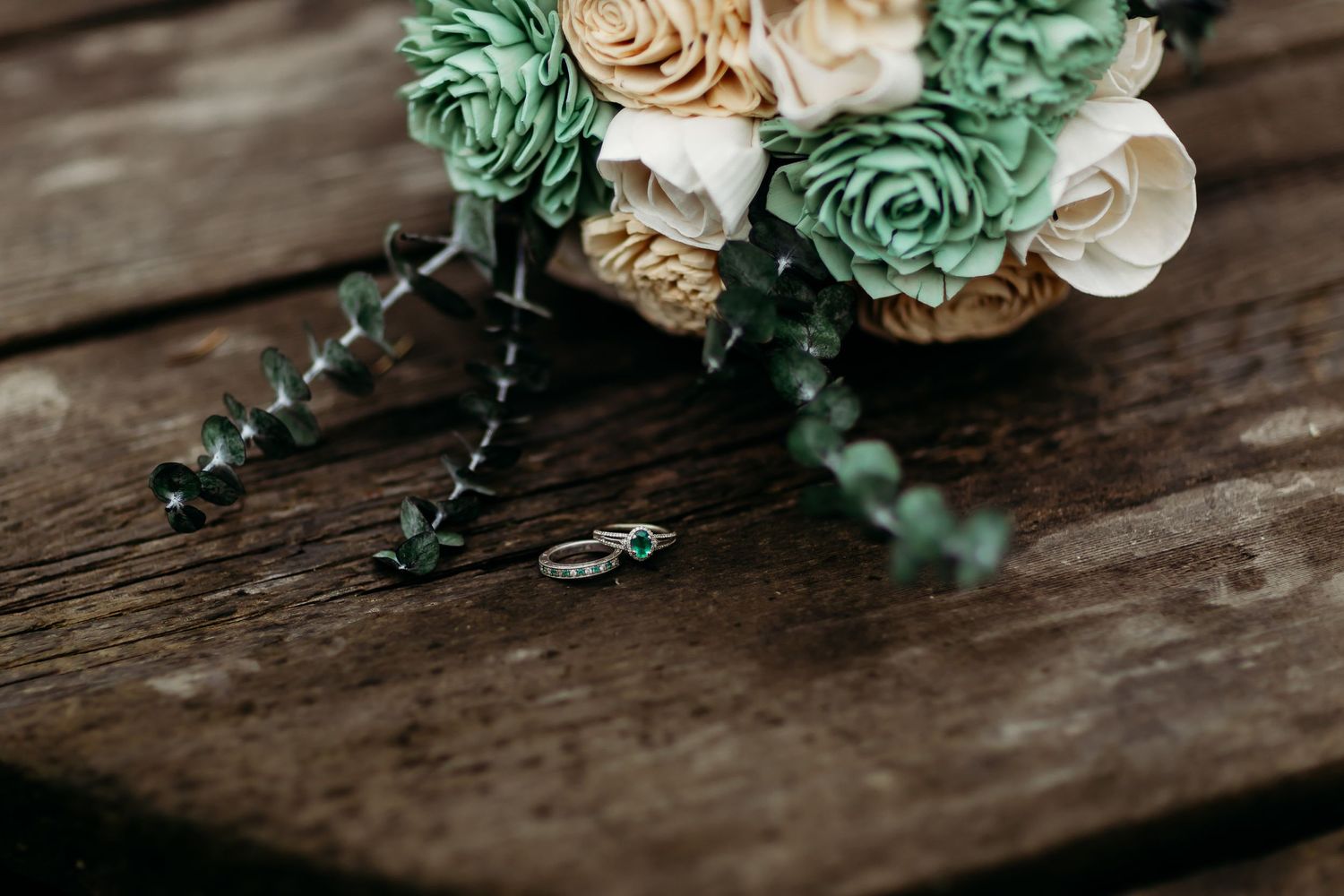 Wedding bouquet with mint green and cream roses on rustic wooden surface.