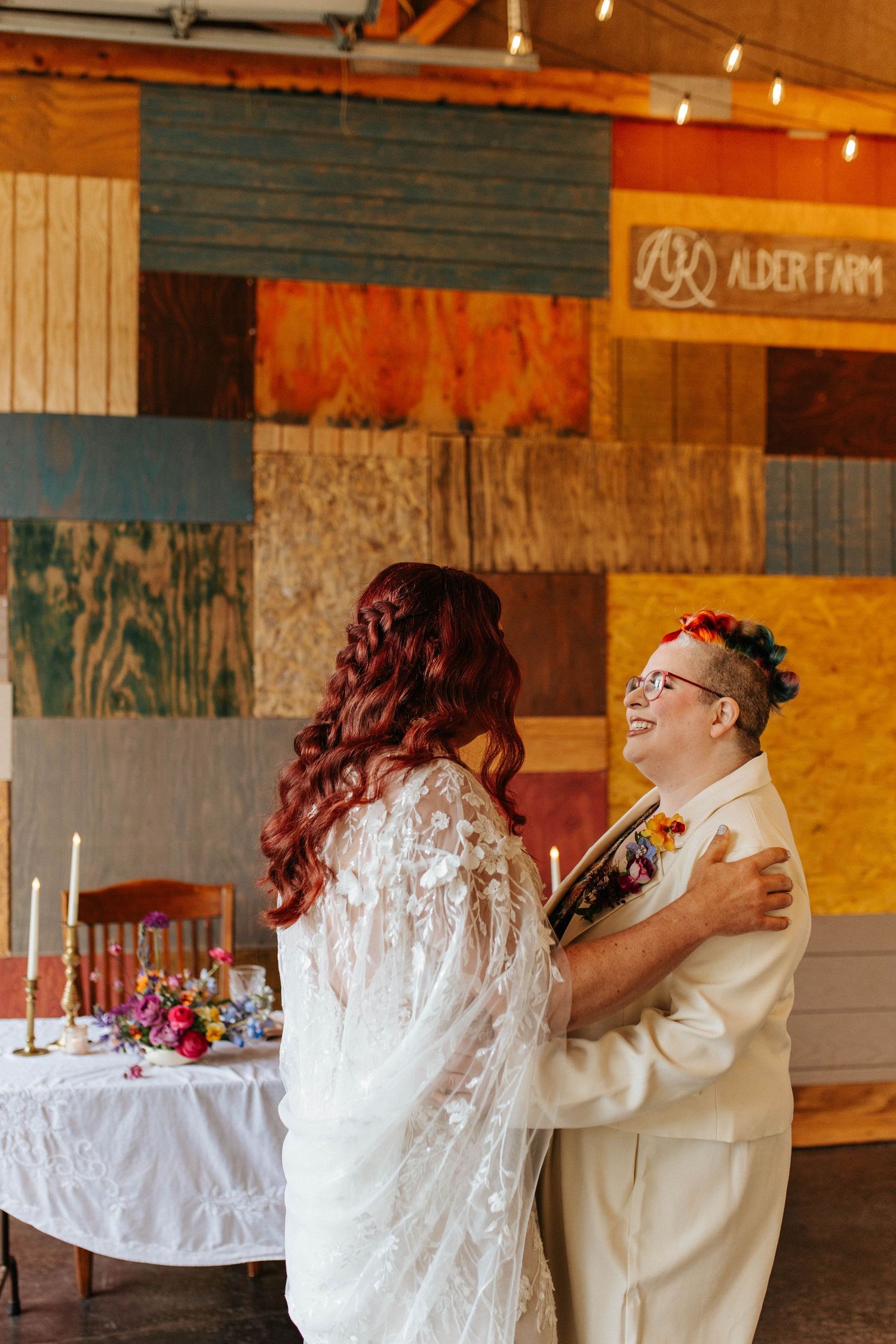 Newlywed couple dances and laughs in rustic barn reception venue with string lights and wood panels.
