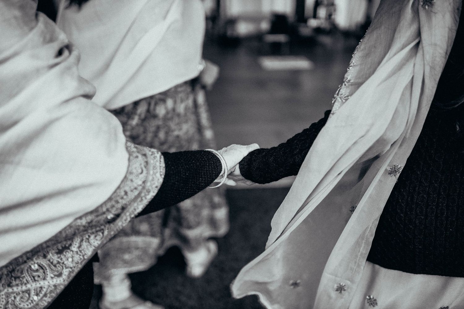 Black and white close-up shot of hands holding traditional wedding attire with intricate details.