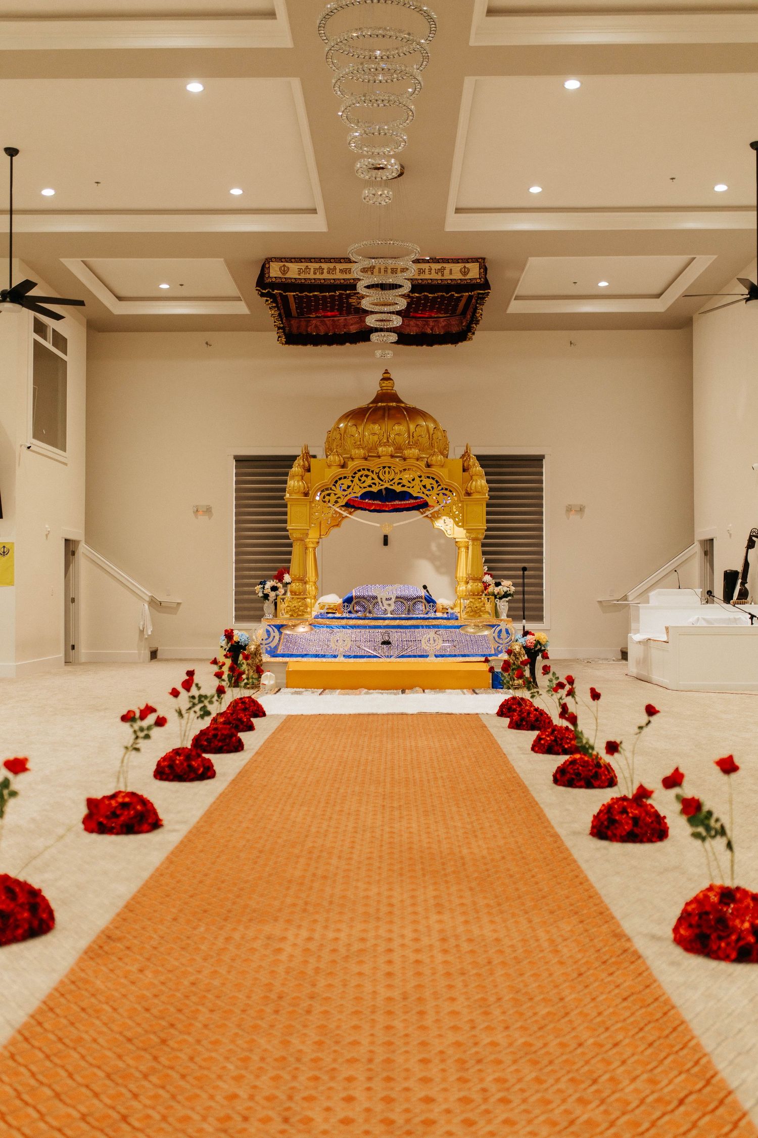 Ceremonial hall with orange carpet runner leading to golden canopy and crystal chandelier.
