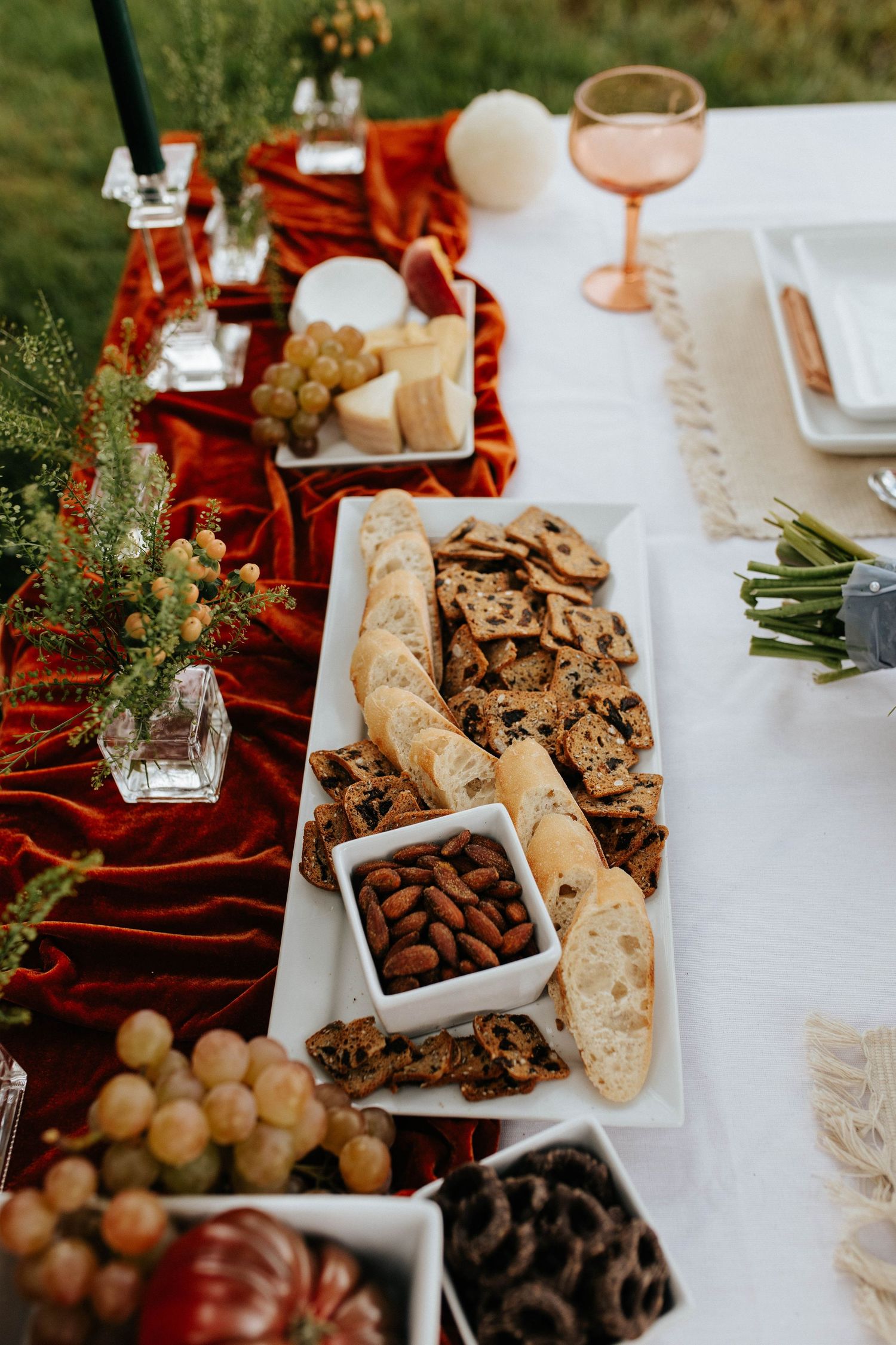 Festive holiday table setting with charcuterie board featuring bread, almonds, grapes and greenery on red velvet runner.