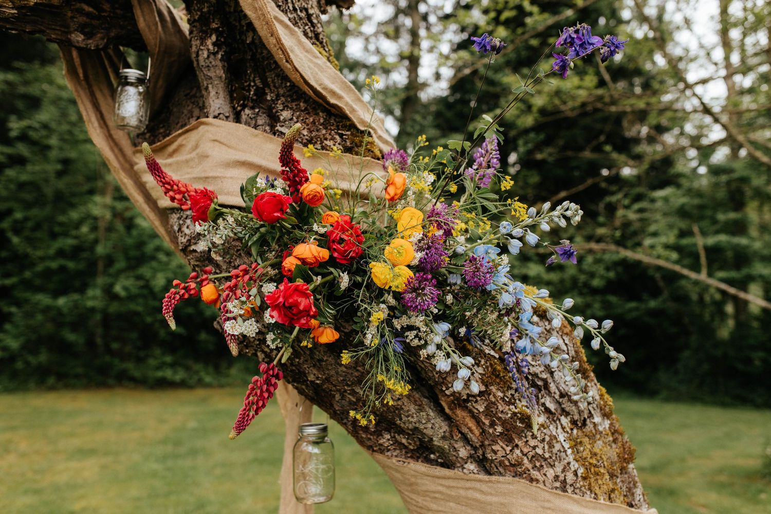 Colorful wildflower arrangement with red and purple blooms decoratively placed on rustic driftwood in an outdoor garden setting.