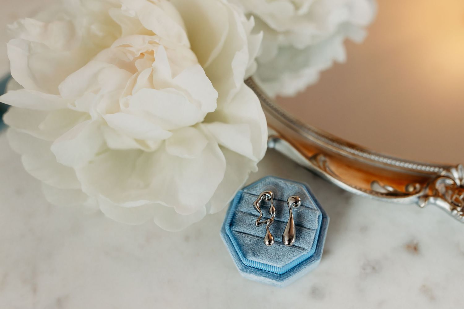 Wedding rings displayed on a light blue octagonal holder beside white flowers.