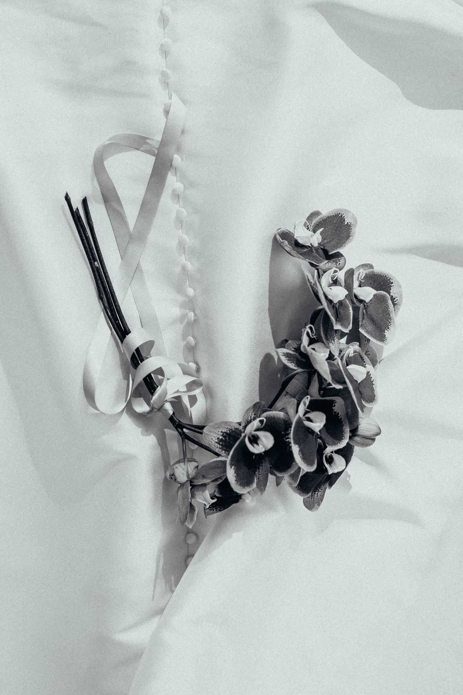 Black and white close-up of floral hair accessories and ribbon resting on a white wedding dress.
