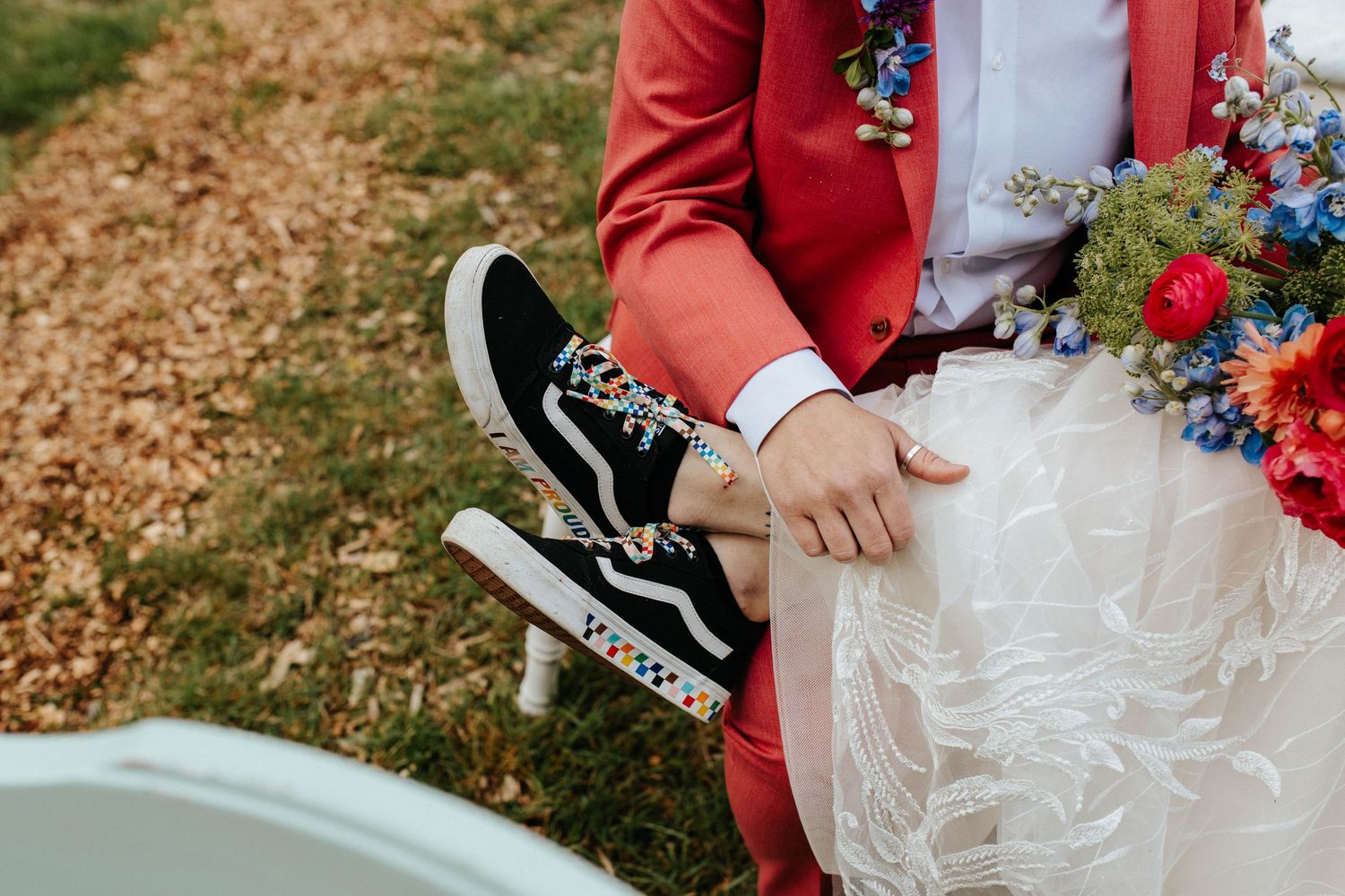 A couple holds hands during an outdoor autumn wedding ceremony featuring bright red and blue floral accents.