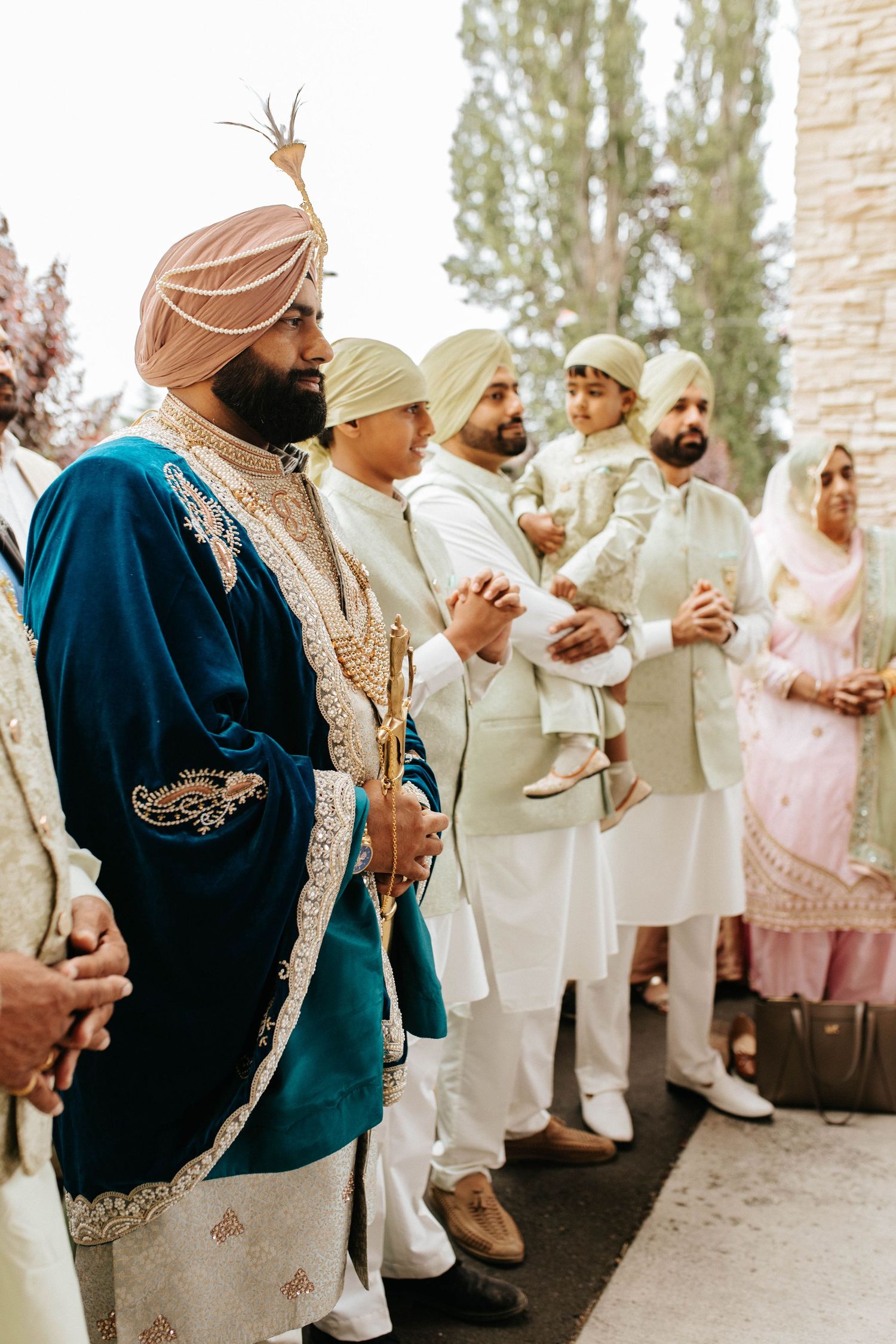 Wedding guests in traditional Sikh attire gathering outdoors, wearing turbans and formal ethnic clothing.