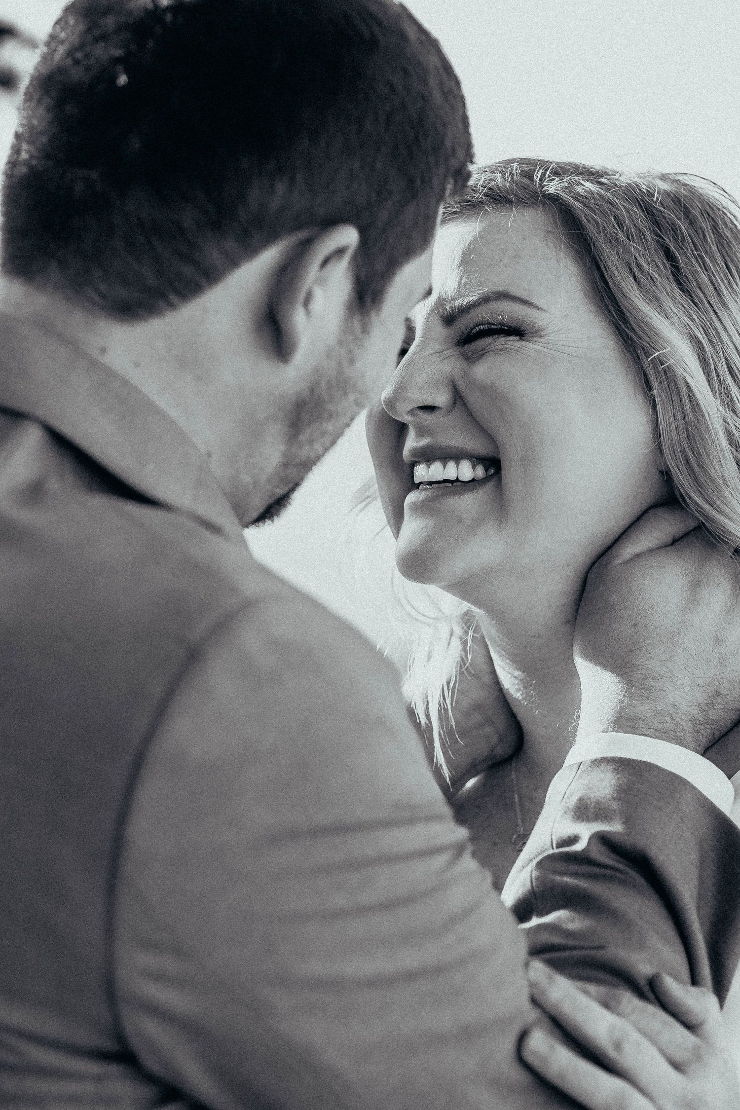 A close-up black and white photo of a joyful couple sharing an intimate laughing moment together.
