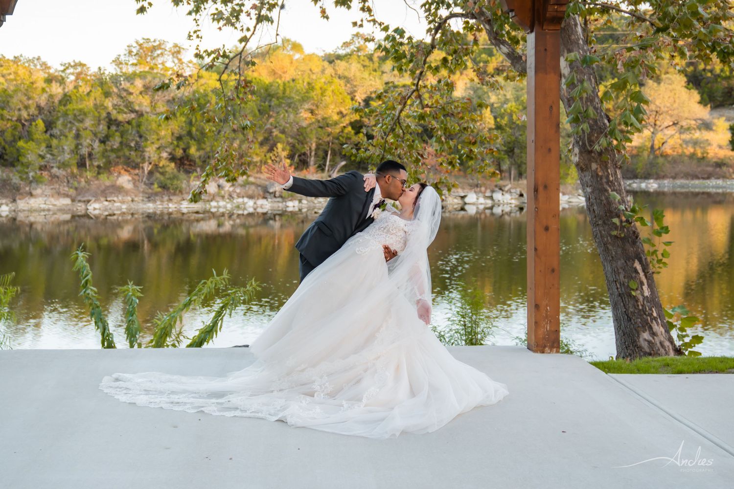 Wedding couple kissing on a white pavilion beside a river at sunset