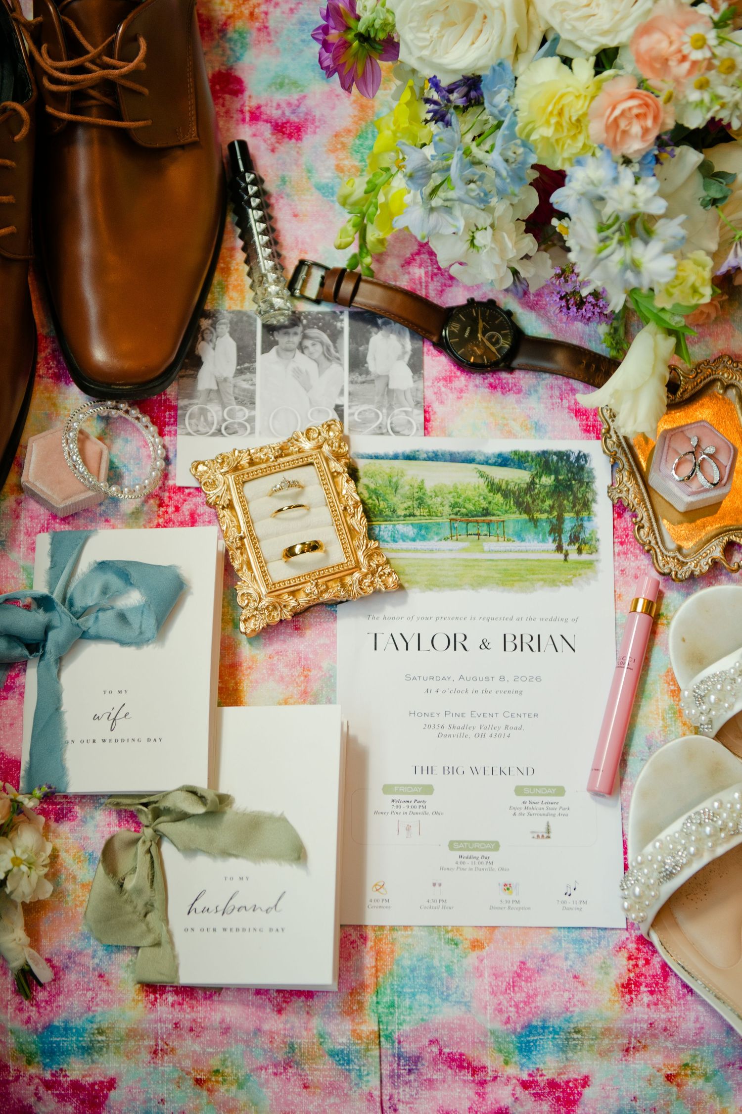 Elegant wedding flat lay with floral bouquet, gold rings, invitations for Taylor and Brian, brown shoes, and colorful backdrop.