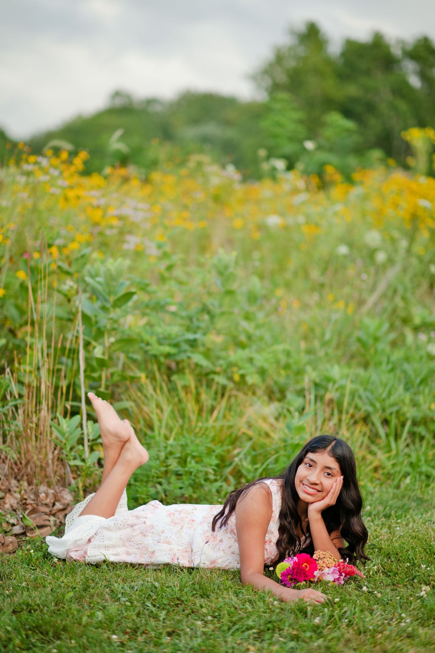 Young woman in floral dress lying on grass in front of a wildflower garden.
