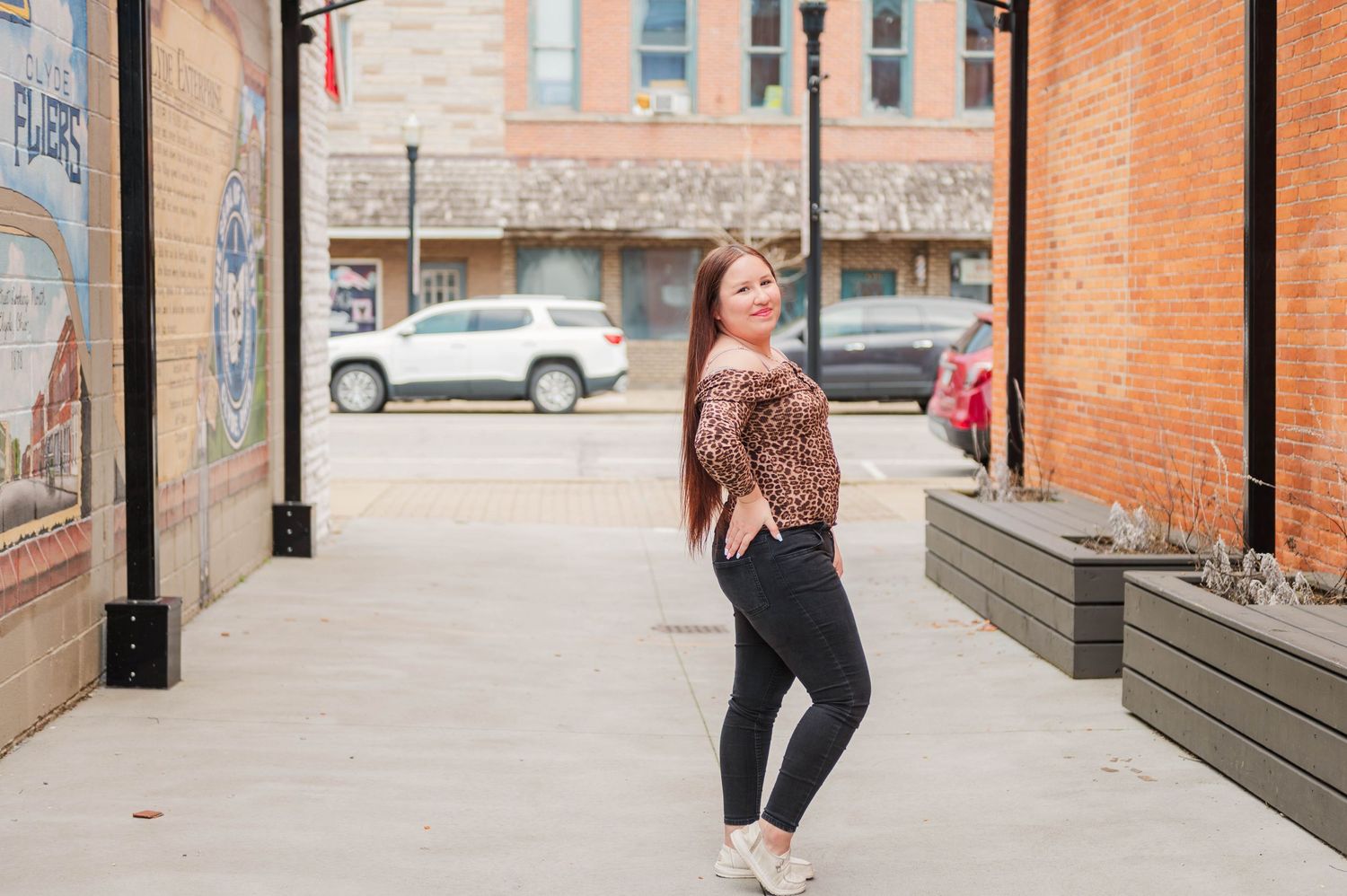 Young woman in leopard print top and black leggings posing on a sidewalk in a small town downtown area.