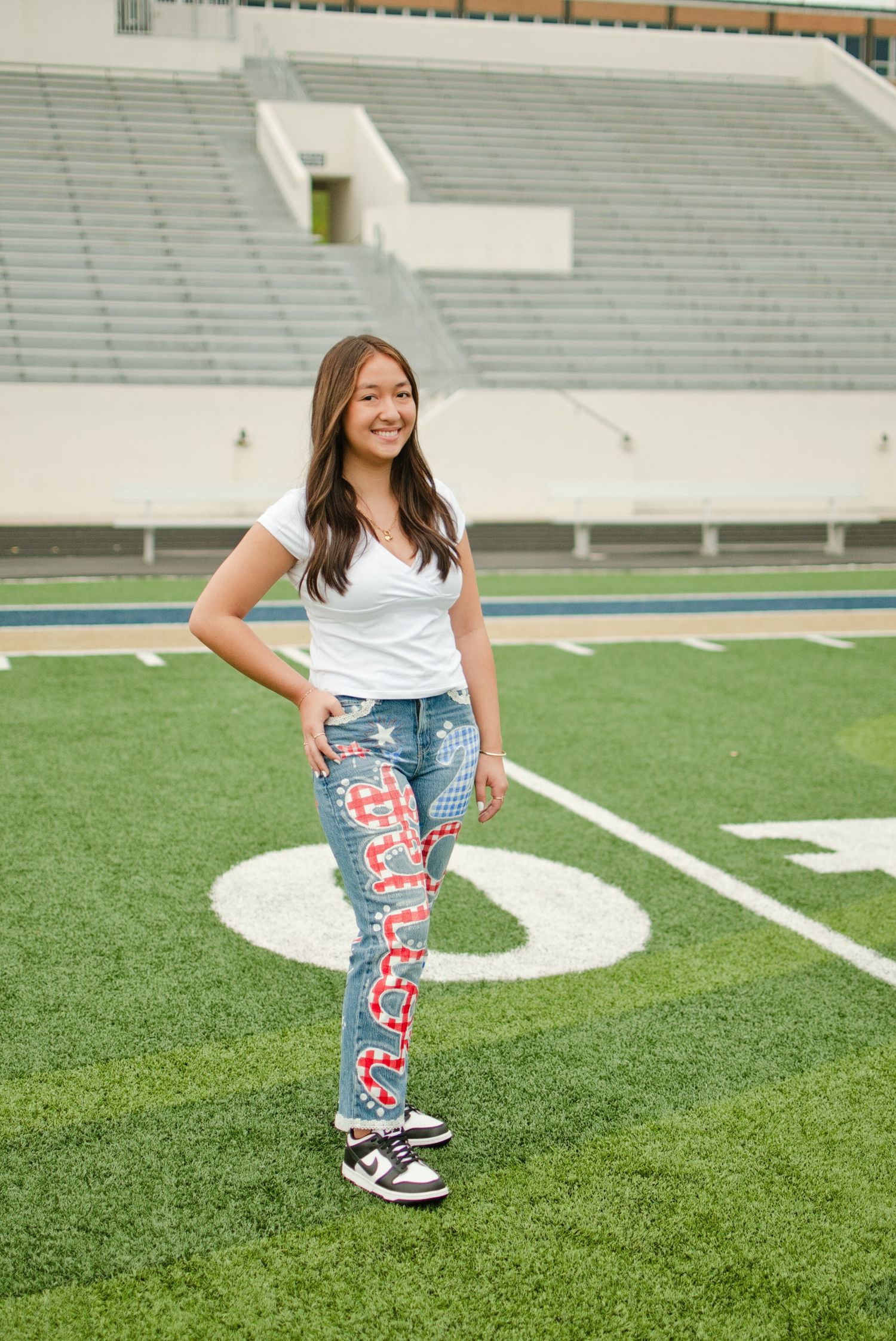 Smiling teen girl poses on football field in white tee and custom red graphic painted jeans.