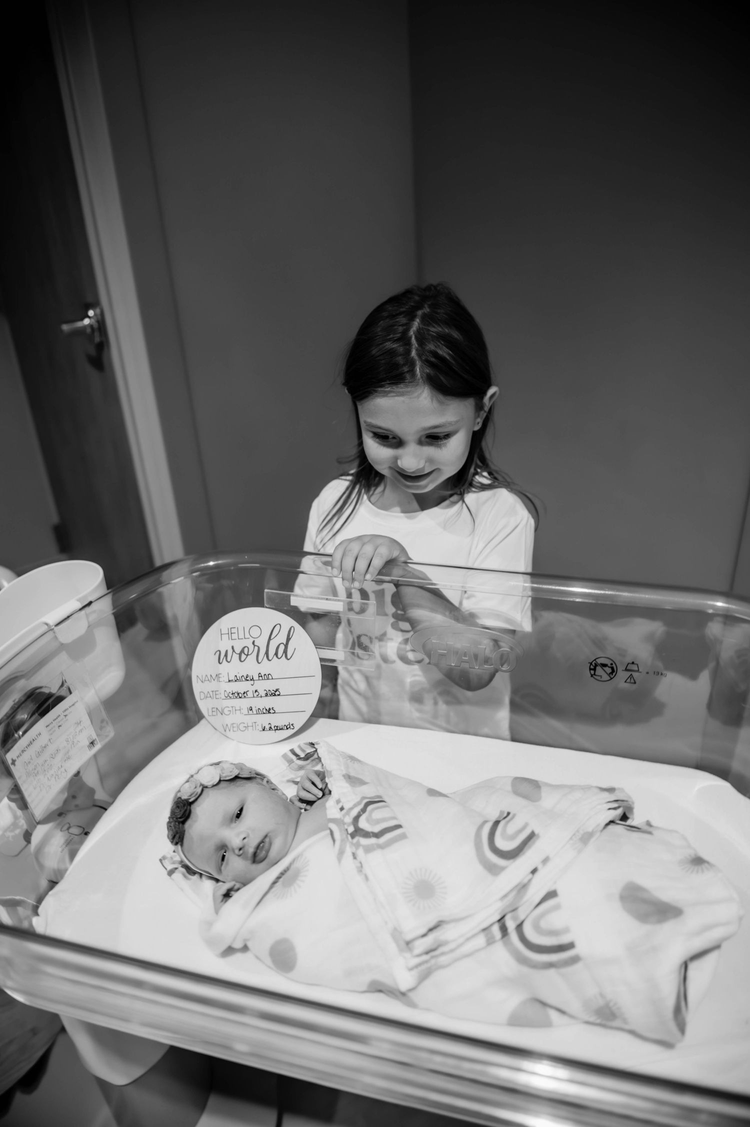 A young child peers into a hospital bassinet containing a newborn.