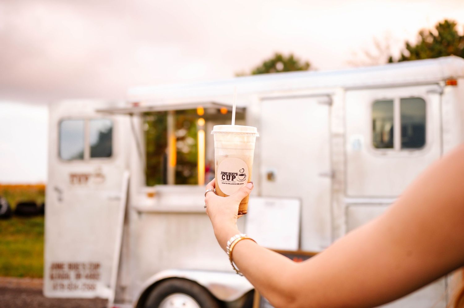 Row of white food trucks parked on gravel with menu signs visible.