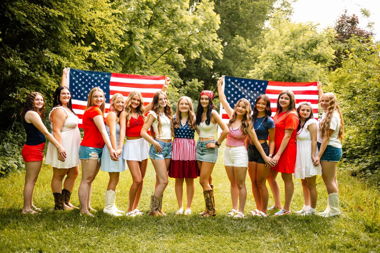 Large group poses with American flags in outdoor summer setting.