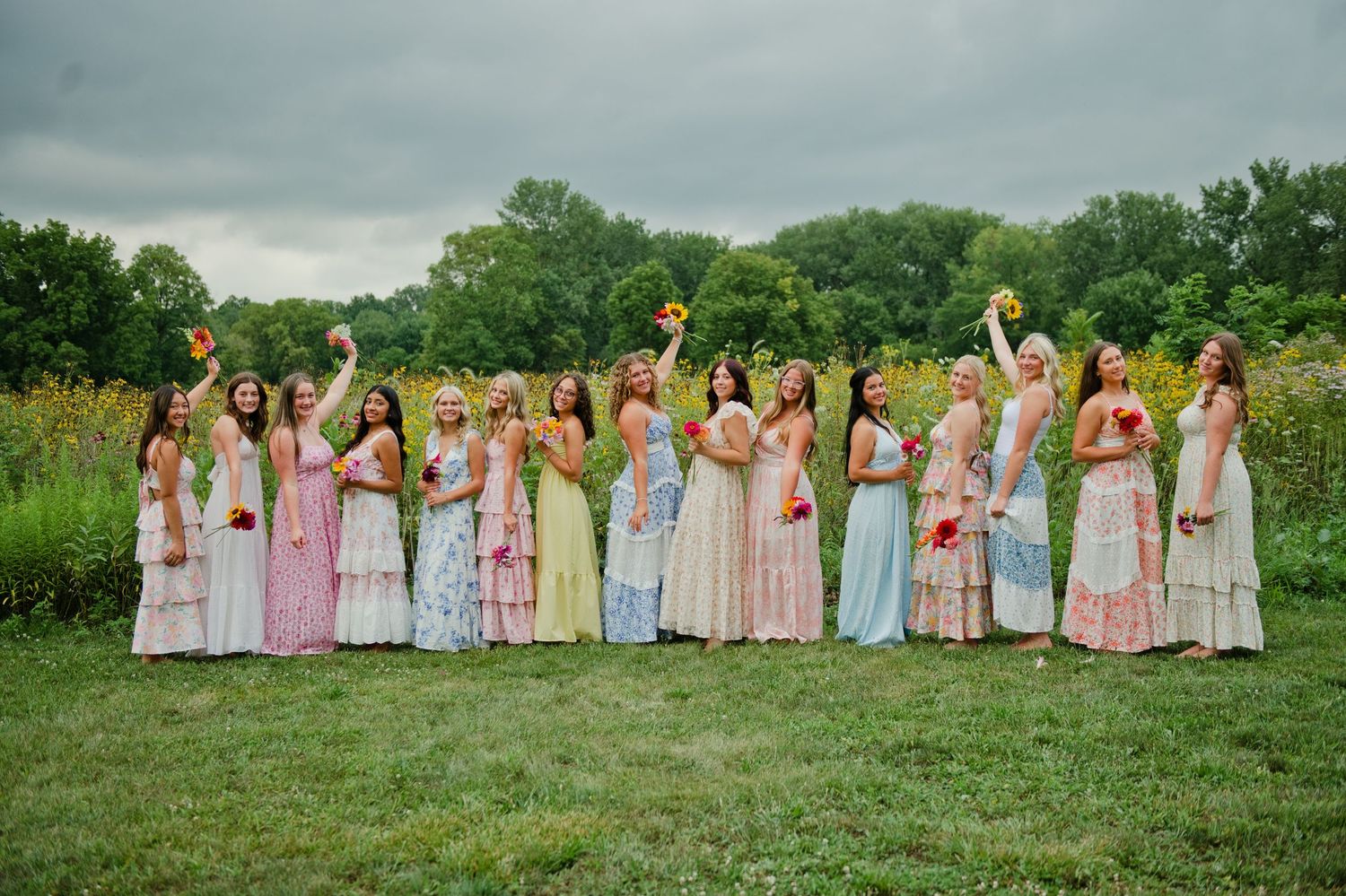 Bridesmaids in mismatched pastel dresses holding colorful bouquets pose outdoors on a green lawn.