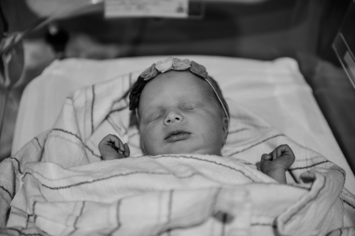A medical bassinet contains a sleeping newborn with monitoring equipment attached.