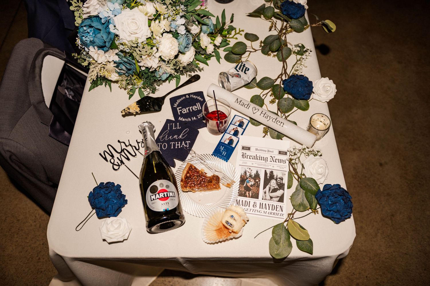 Wedding reception table decorated with blue flowers and scattered photographs.