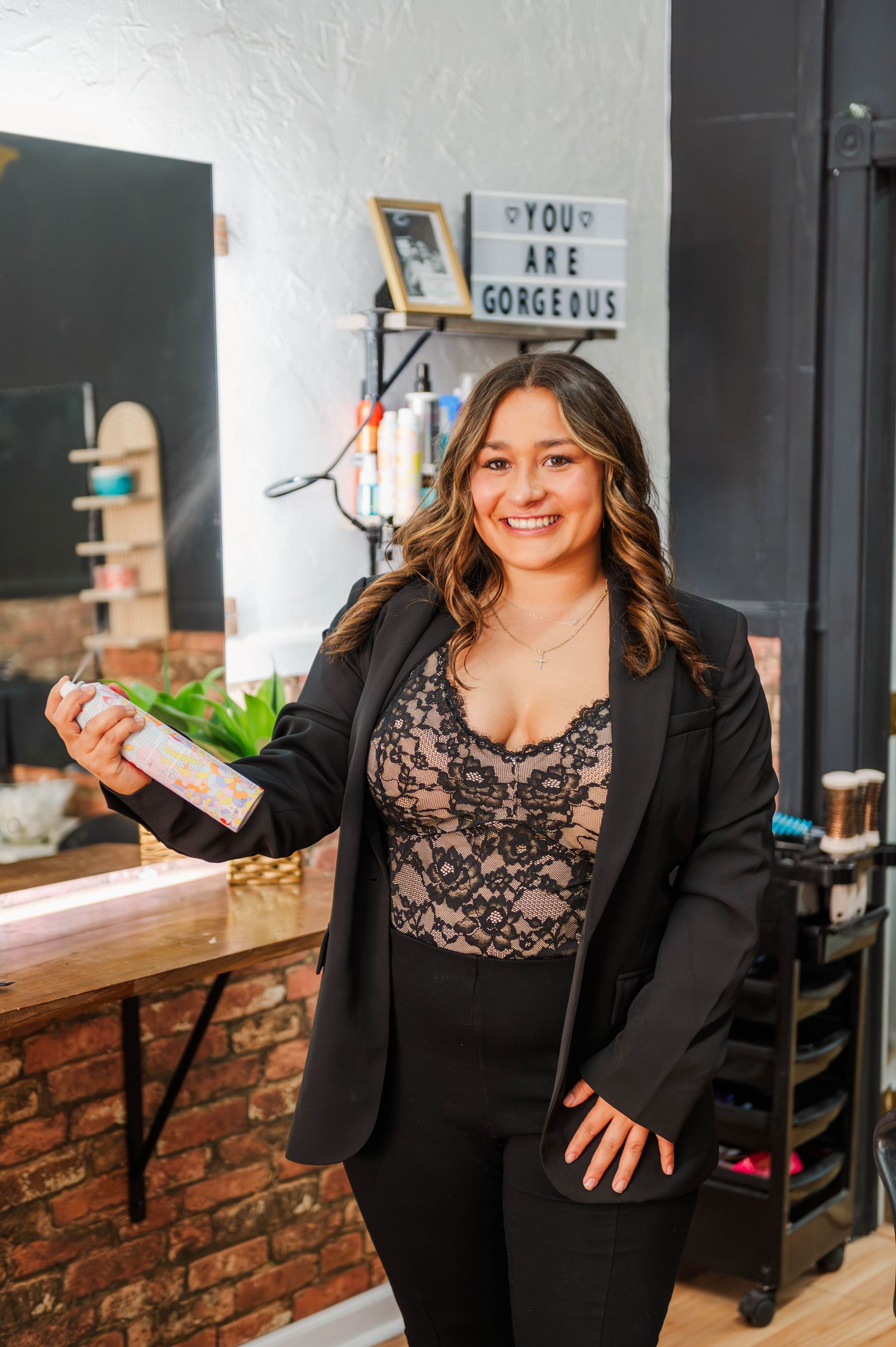 Business professional in black blazer seated at wooden table with brick wall backdrop.