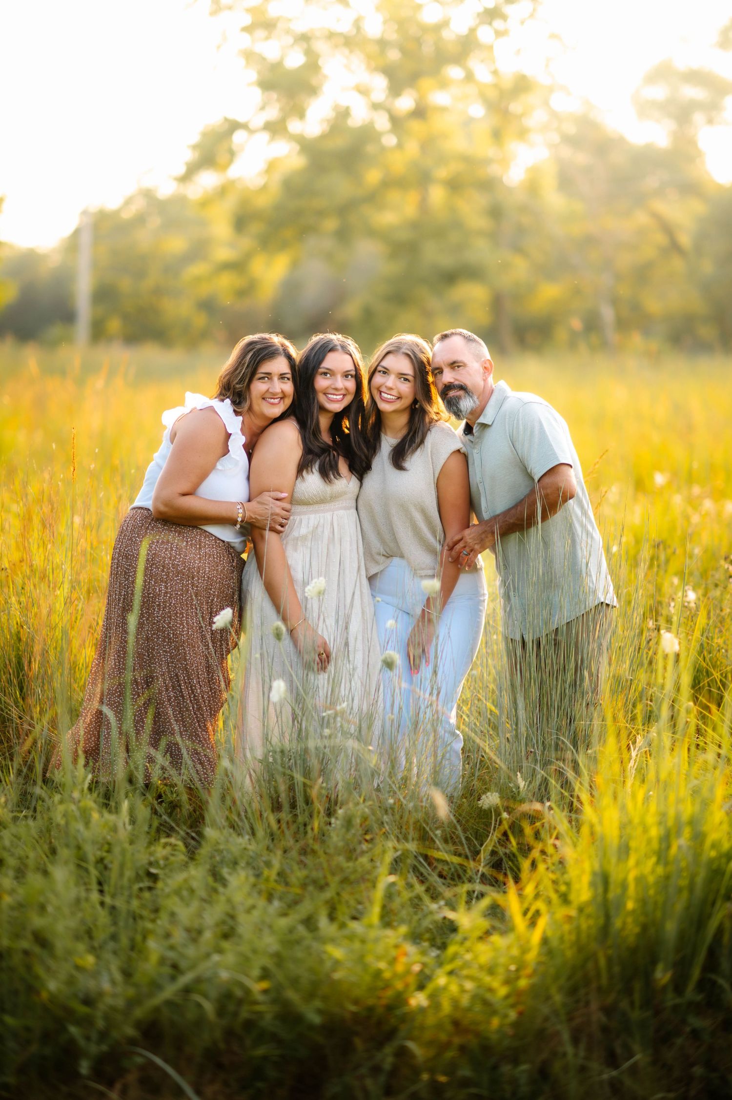A group poses together in a golden sunlit field of tall grass during sunset.