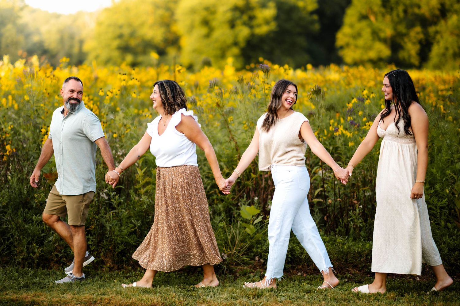 Fun family portrait with coordinated white and tan outfits in a wildflower meadow.
