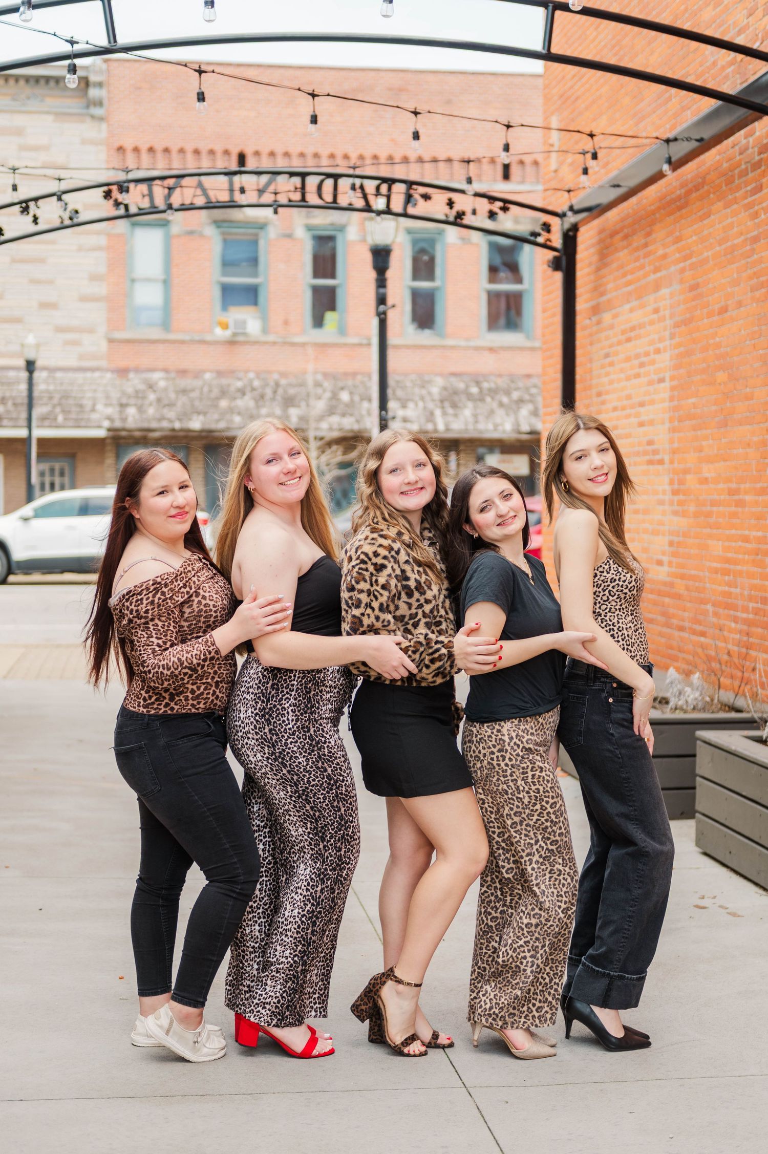 Five young women in leopard print outfits pose together smiling under string lights on an outdoor patio.