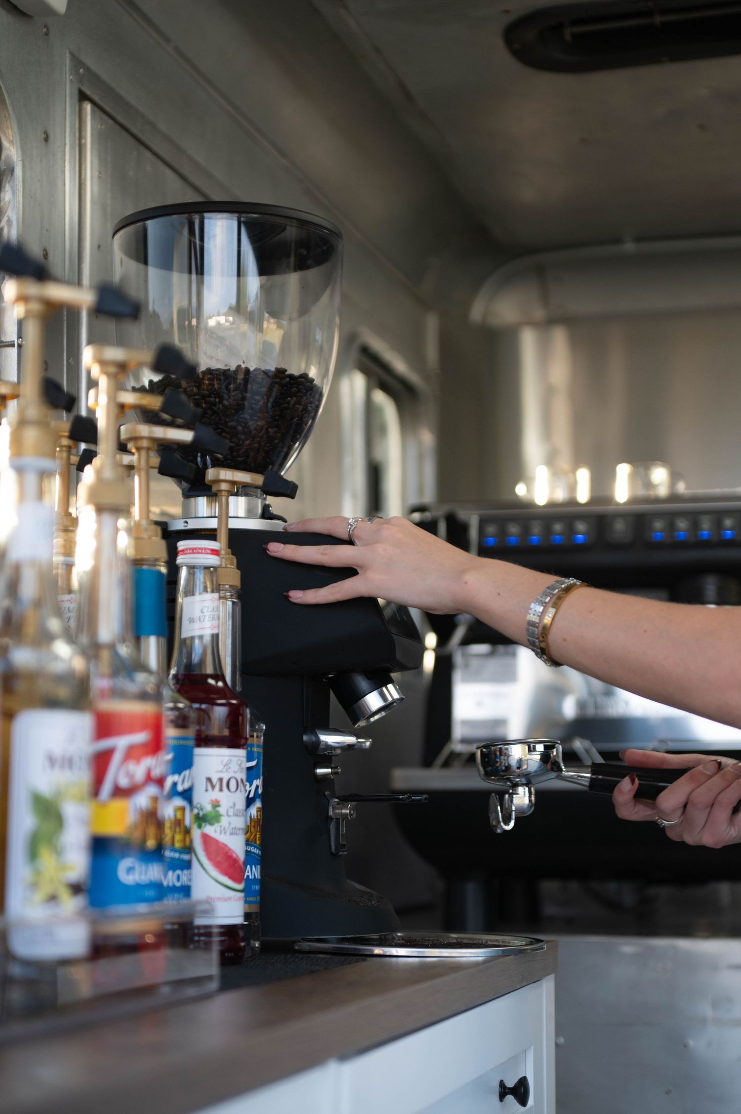 Hand reaching towards commercial coffee equipment in a cafe setting.