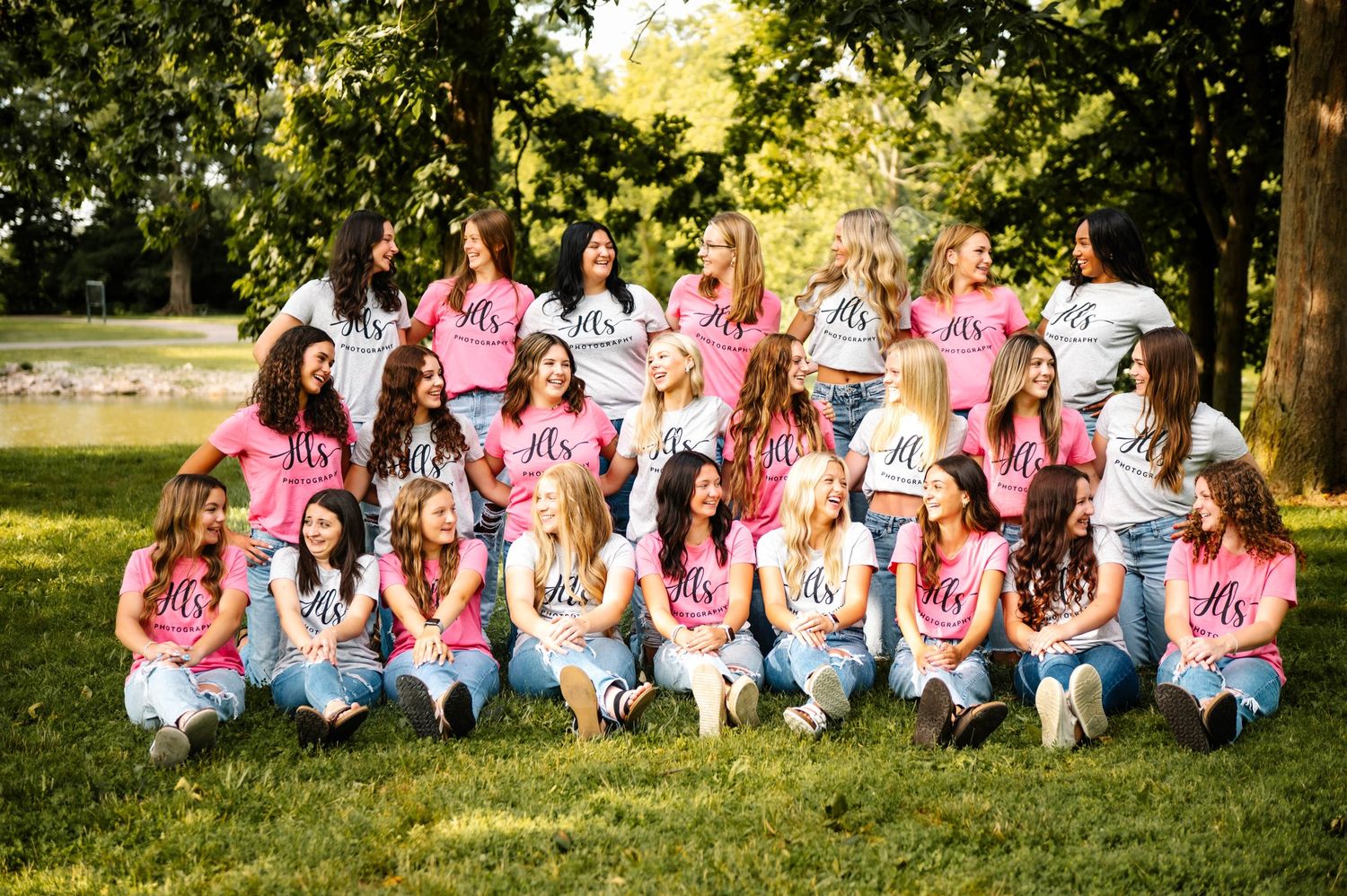 Large group photo of people wearing pink and white shirts sitting on grass in an outdoor setting.