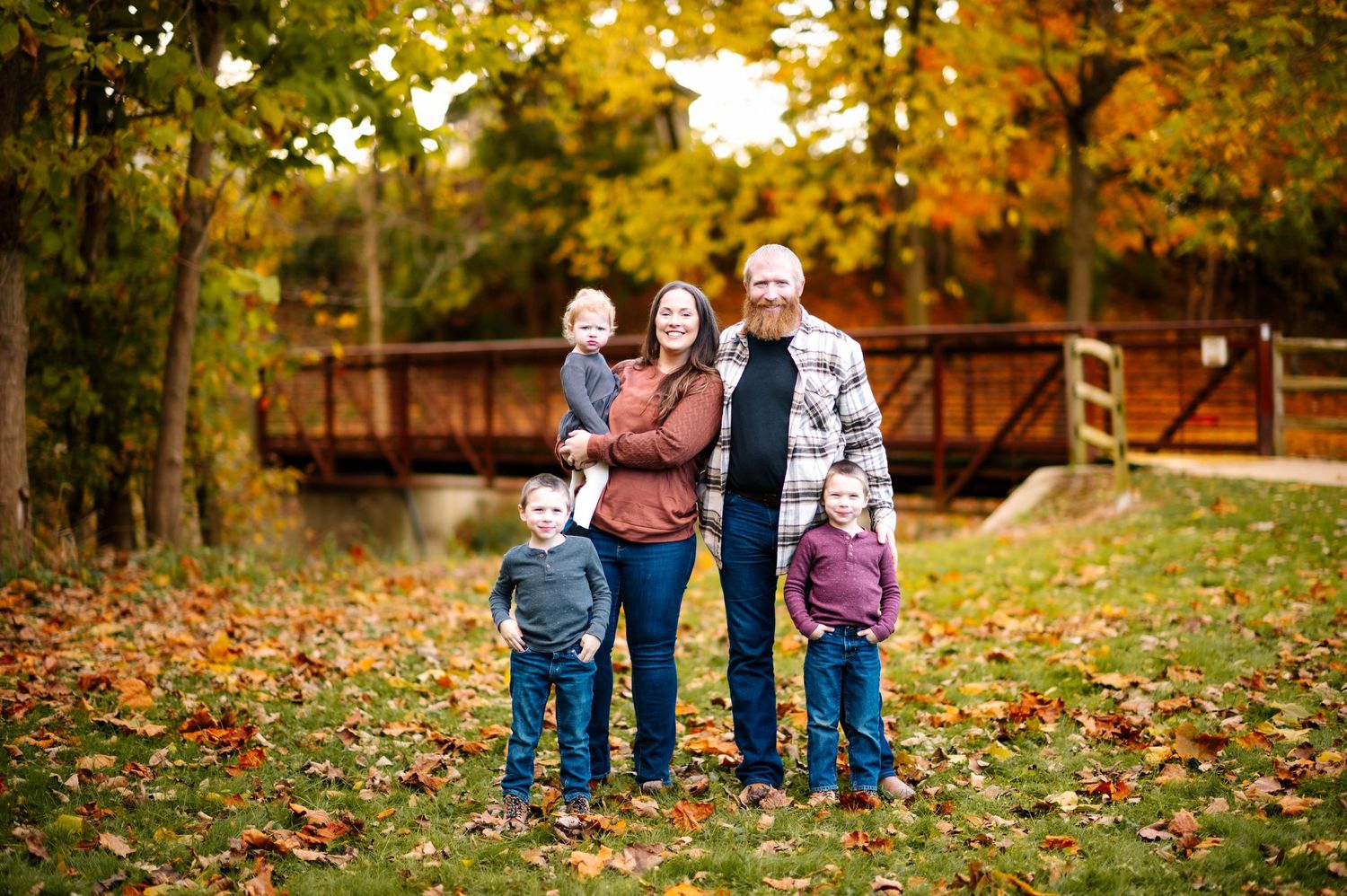 A family poses together in front of a wooden bridge during autumn with colorful fall foliage.