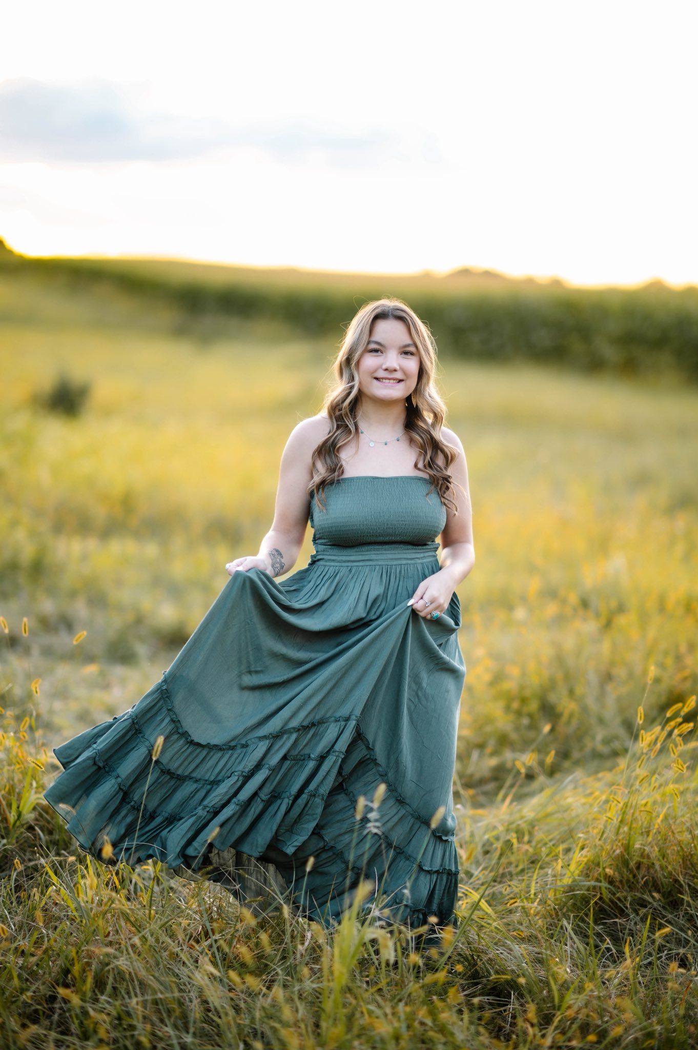 A flowing teal dress swirls gracefully in a golden field at sunset.