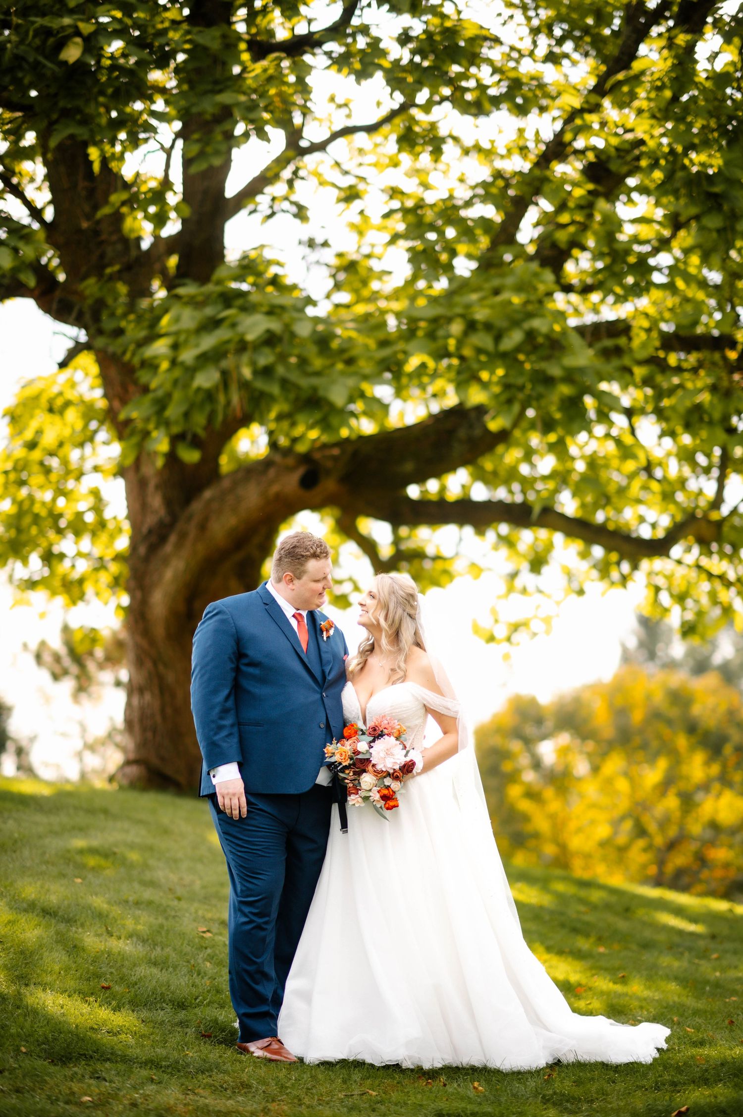Wedding couple shares intimate moments on a grassy hill surrounded by trees at golden hour.