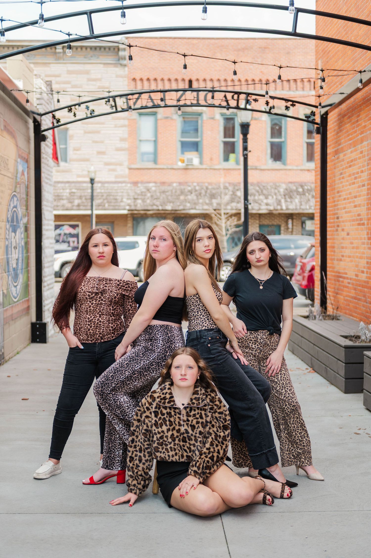 Five young women striking a dramatic pose under an arch in a downtown alley wearing leopard print and black.