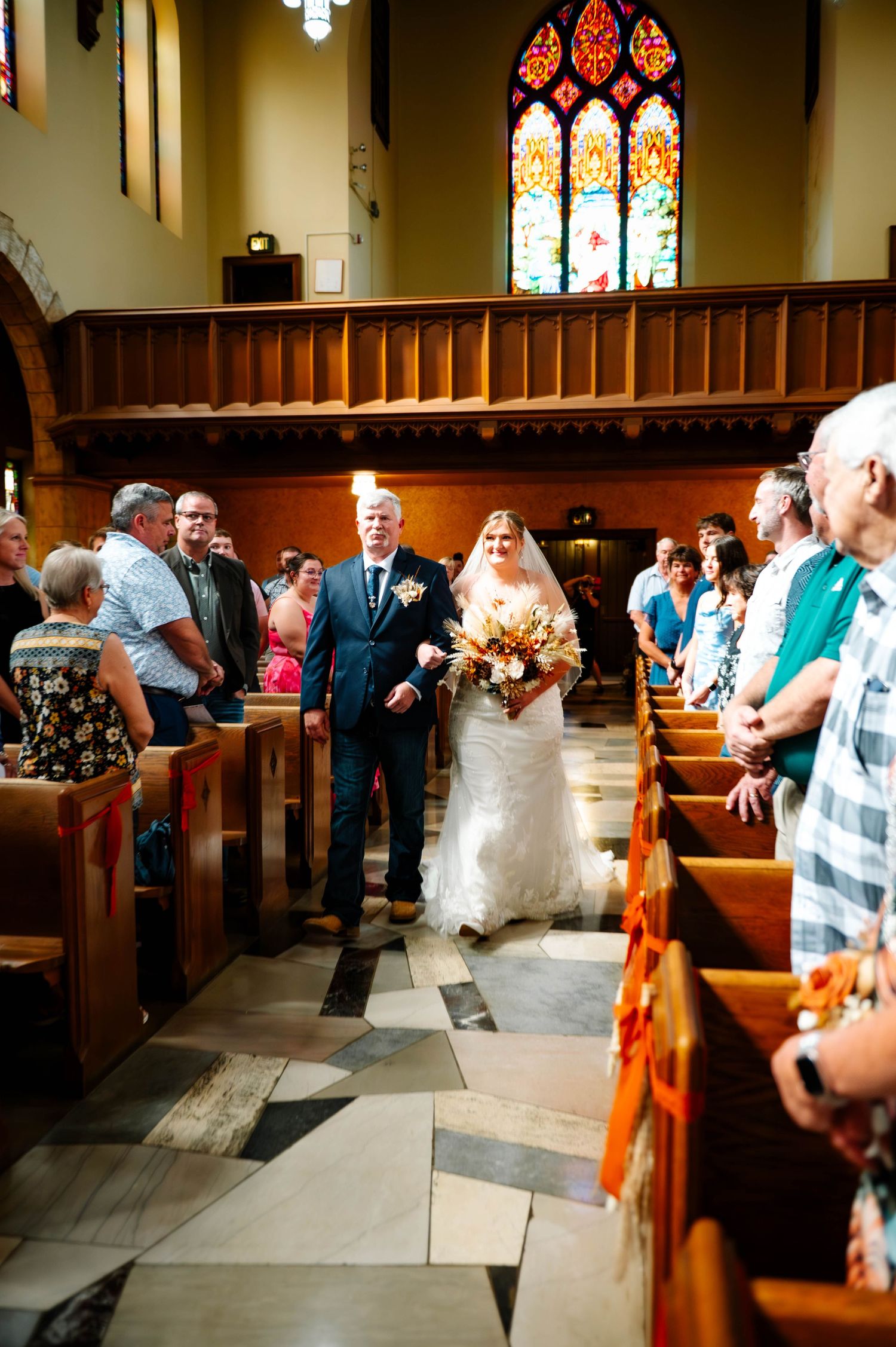 Wedding ceremony in progress inside a historic church with stained glass windows and wooden pews.