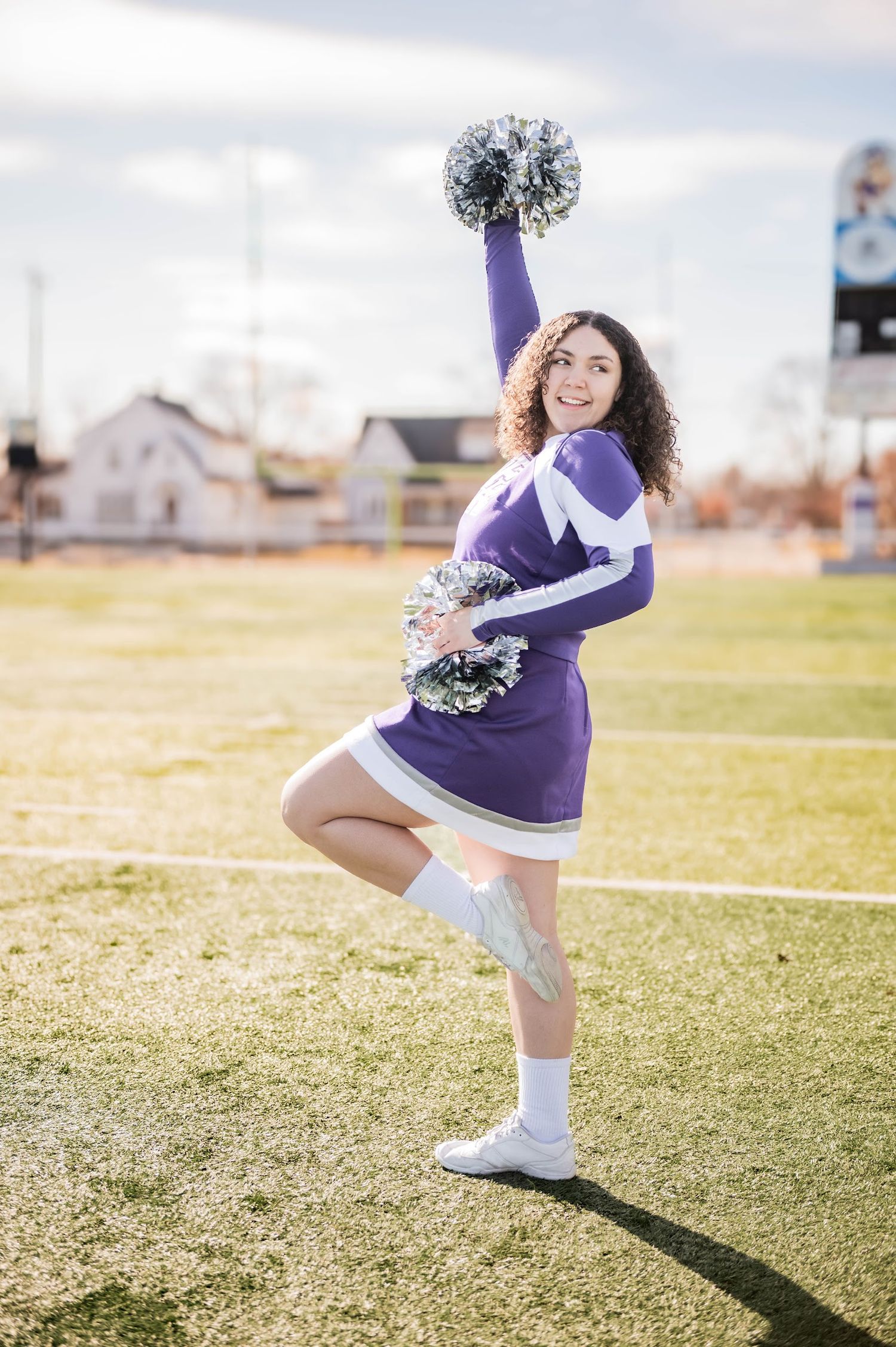 Cheerleader in purple uniform performs dynamic poses on sunny sports field.