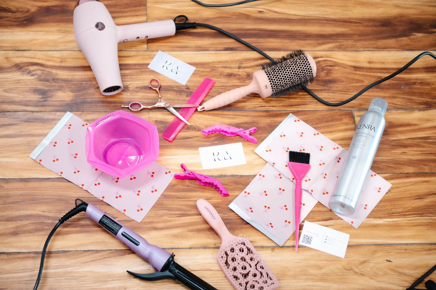 Flatlay of pink and metallic accessories on wooden surface with business cards and styling elements.