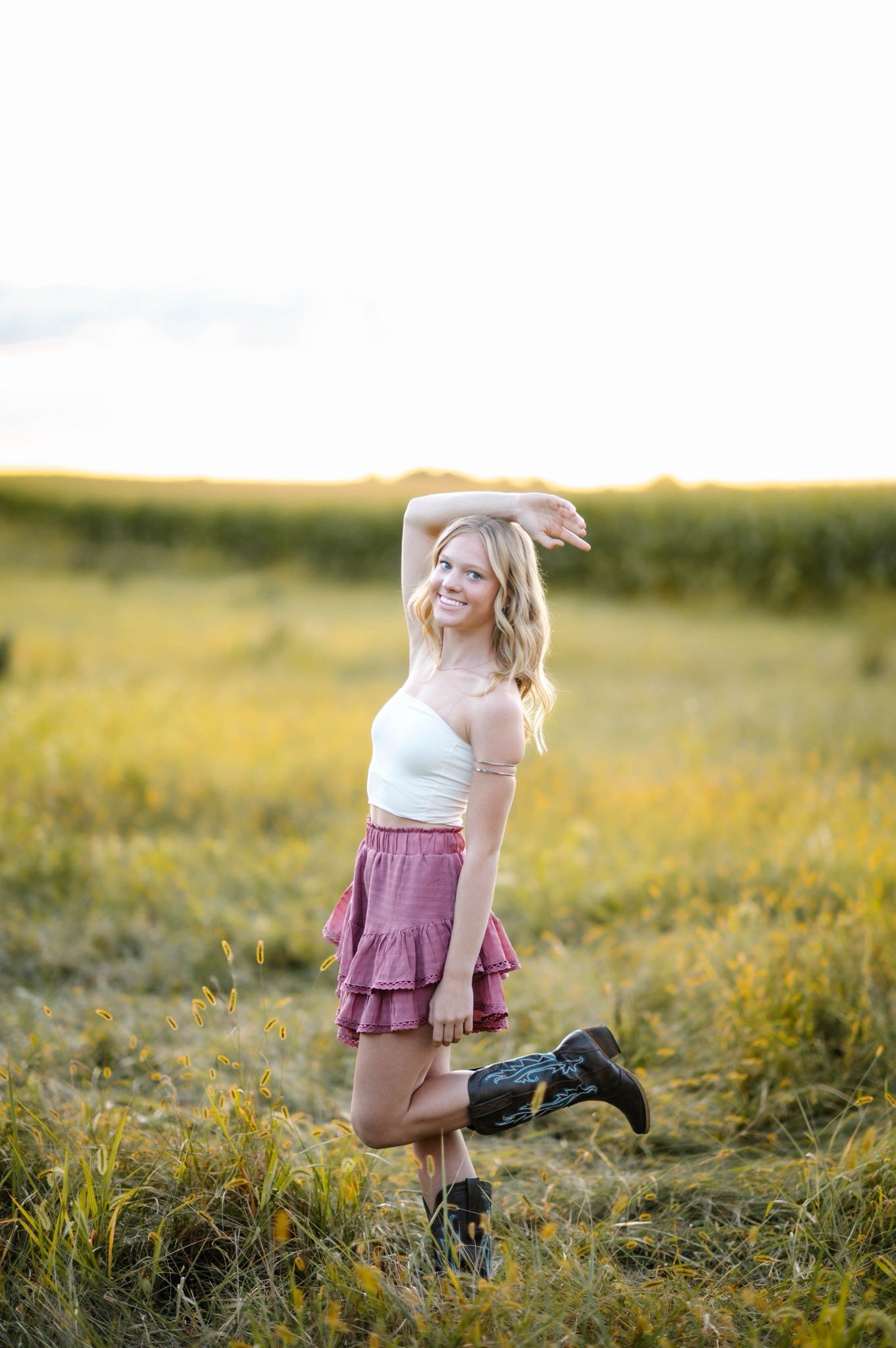 Person in purple skirt posing playfully in sunlit meadow.
