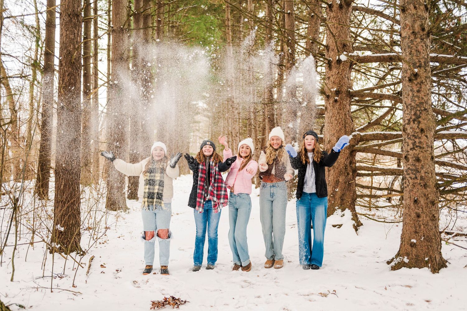 Winter group portrait session among tall evergreen trees with snow on the ground.