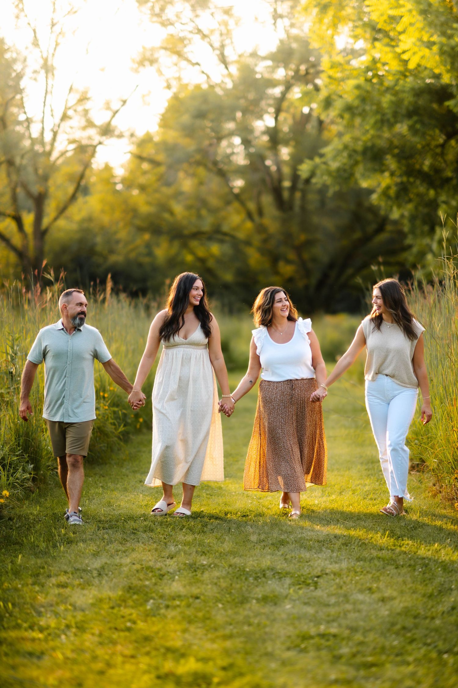 Four people walk hand in hand along a grassy path during golden hour.