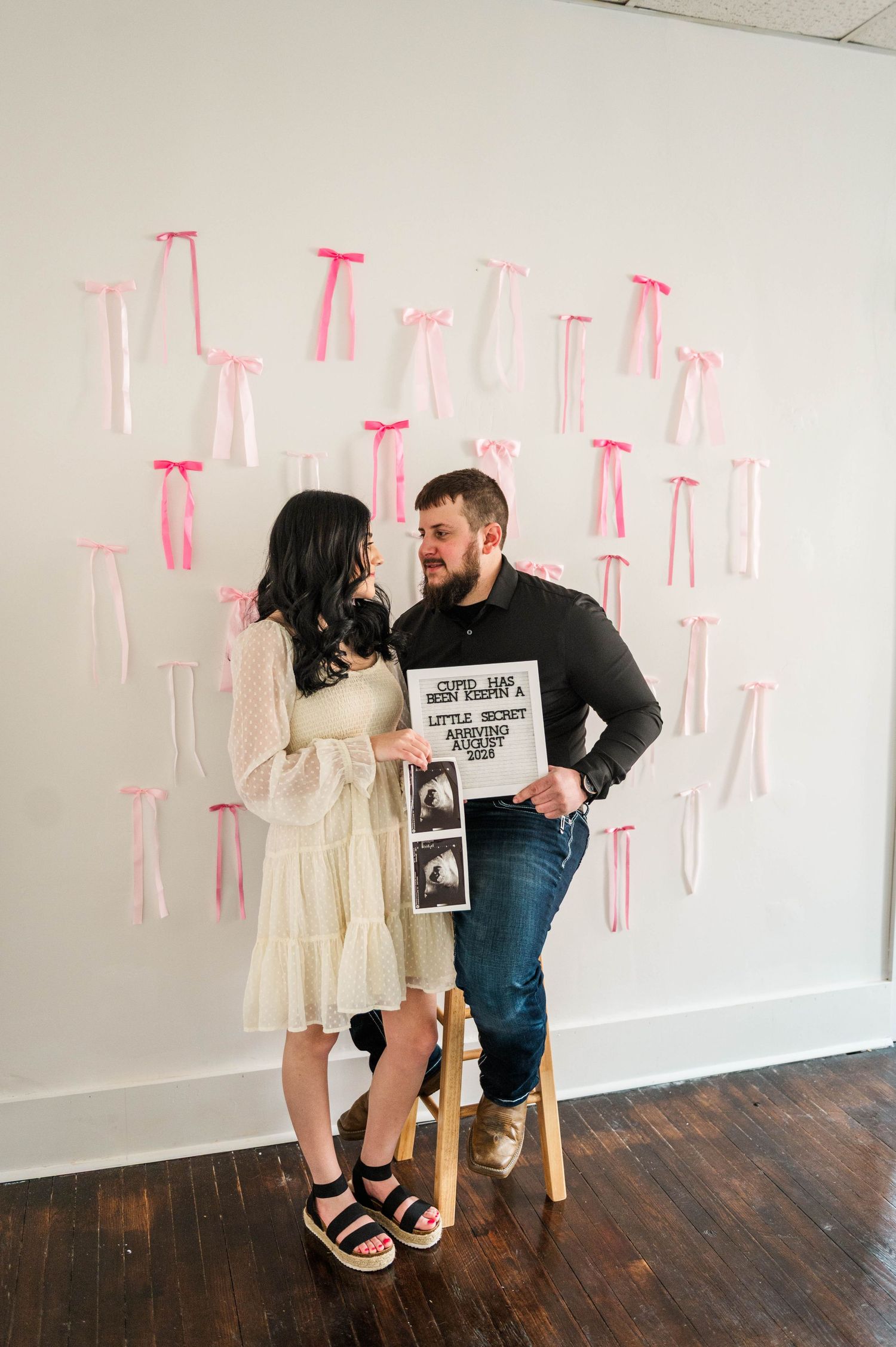 A couple poses playfully with pregnancy announcement signs and ultrasound photos.