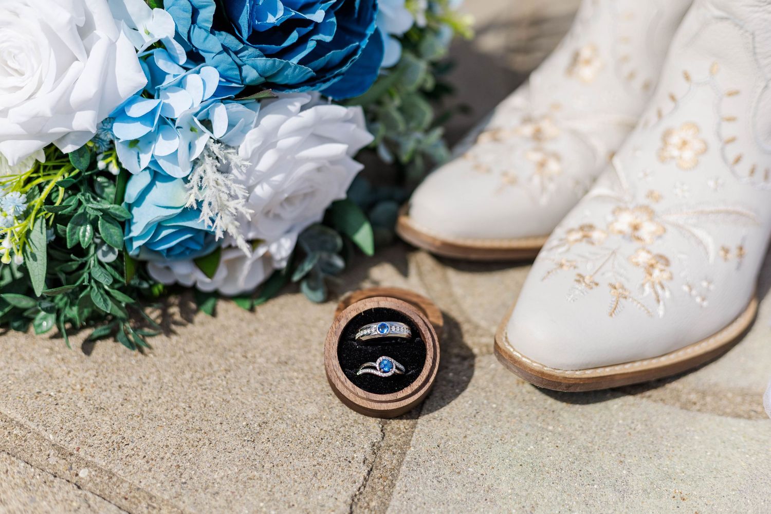 Wedding detail shot of blue floral arrangements and bridal shoes on concrete surface.