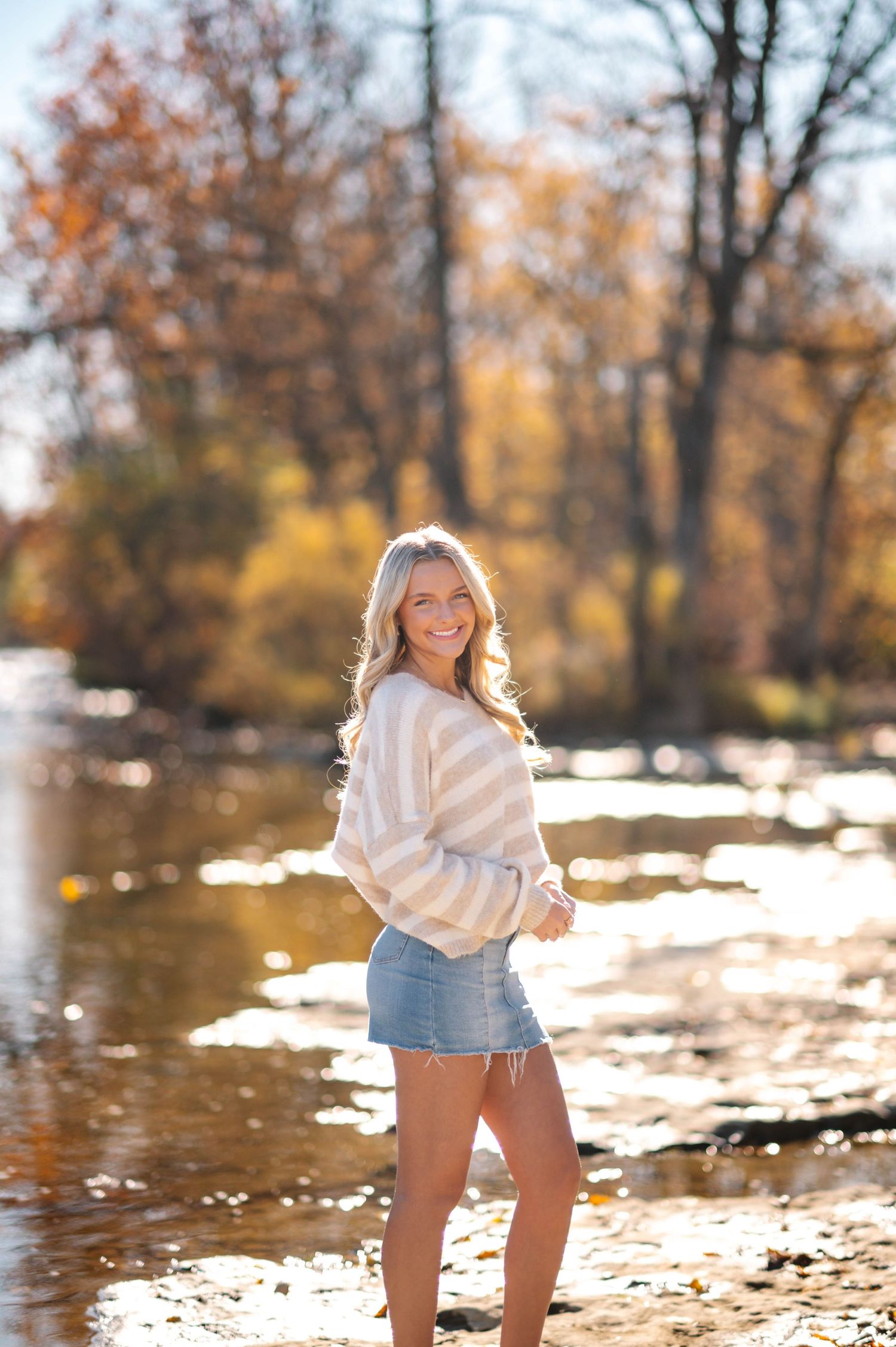 Autumn outdoor photoshoot near a lake with fallen leaves and golden sunlight.