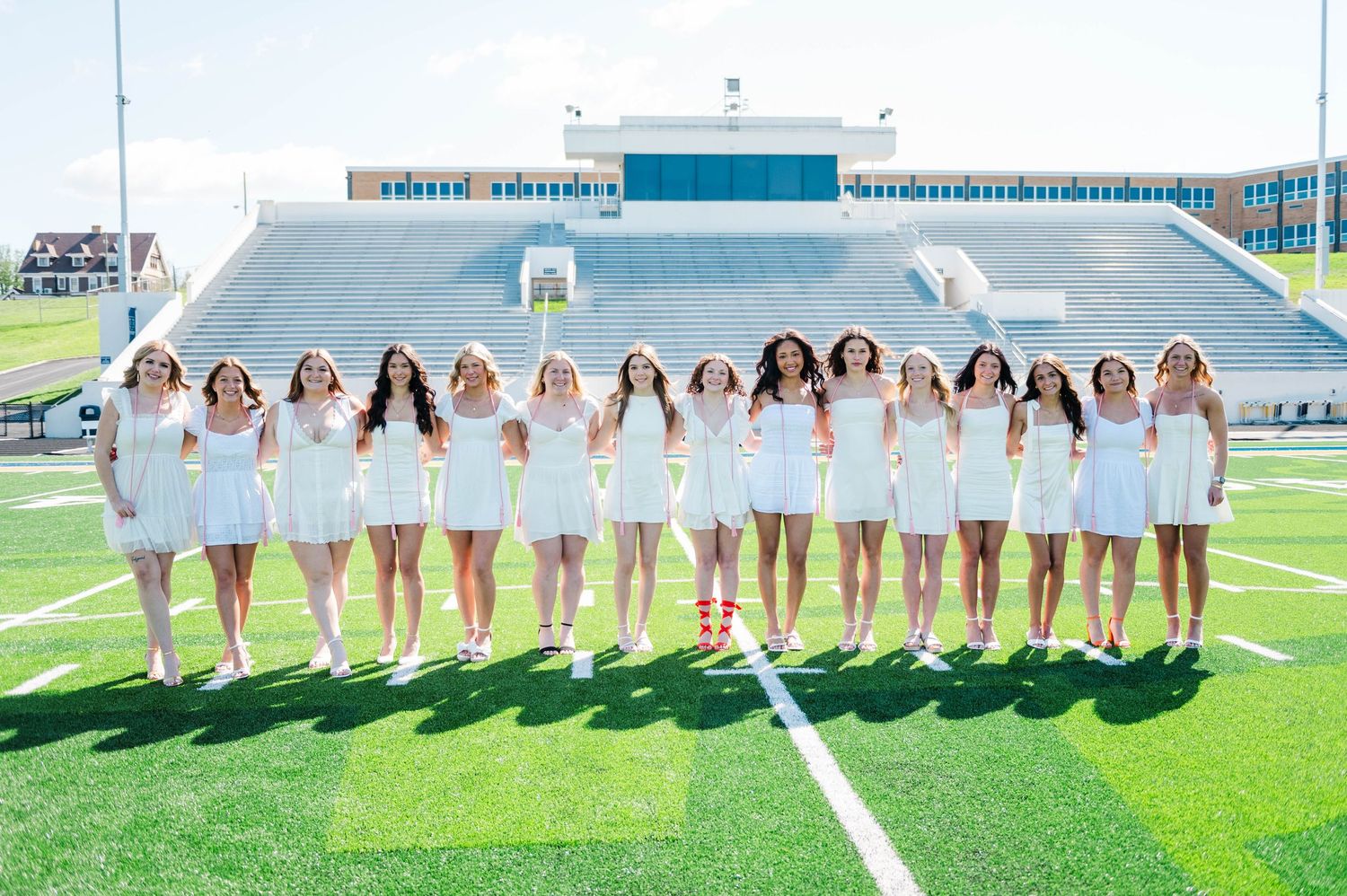 Group of young women in white dresses posing on a football field for a graduation photo shoot.
