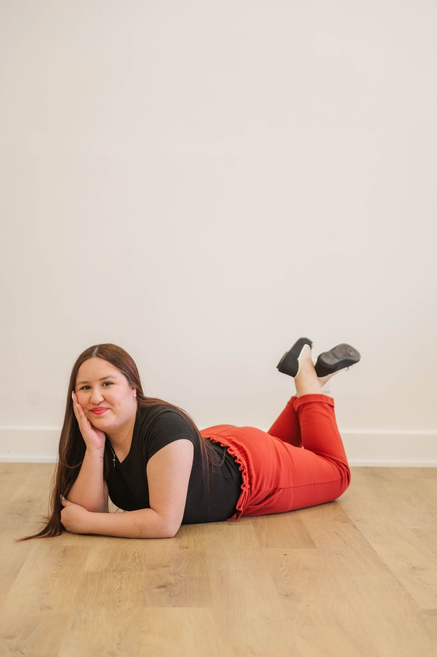 Woman in black top and red pants lying on hardwood floor in relaxed pose.