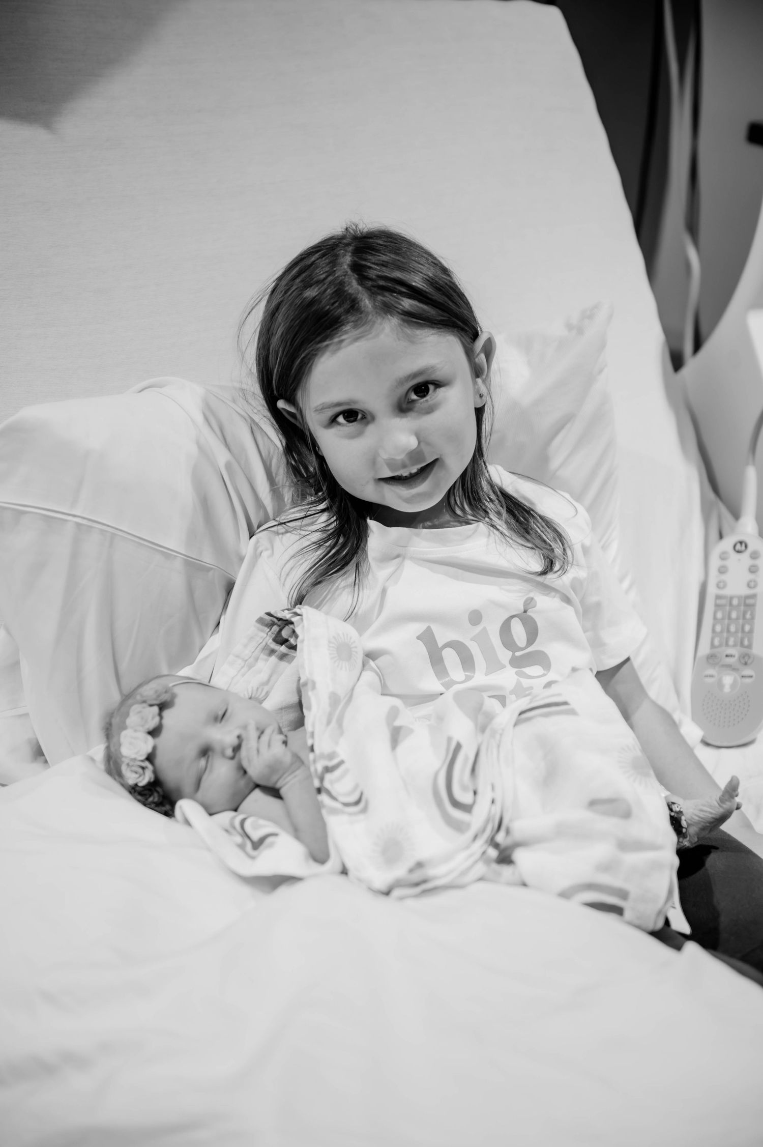 A child lies on hospital bedding while looking at a newborn sibling.