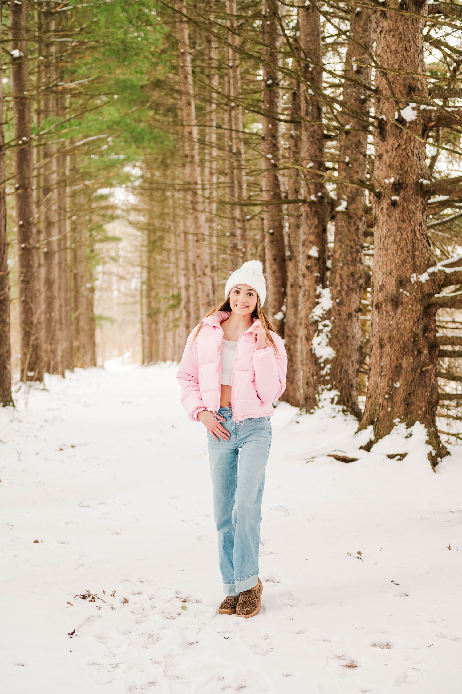 Pink winter jacket and denim outfit styled against snowy forest backdrop.