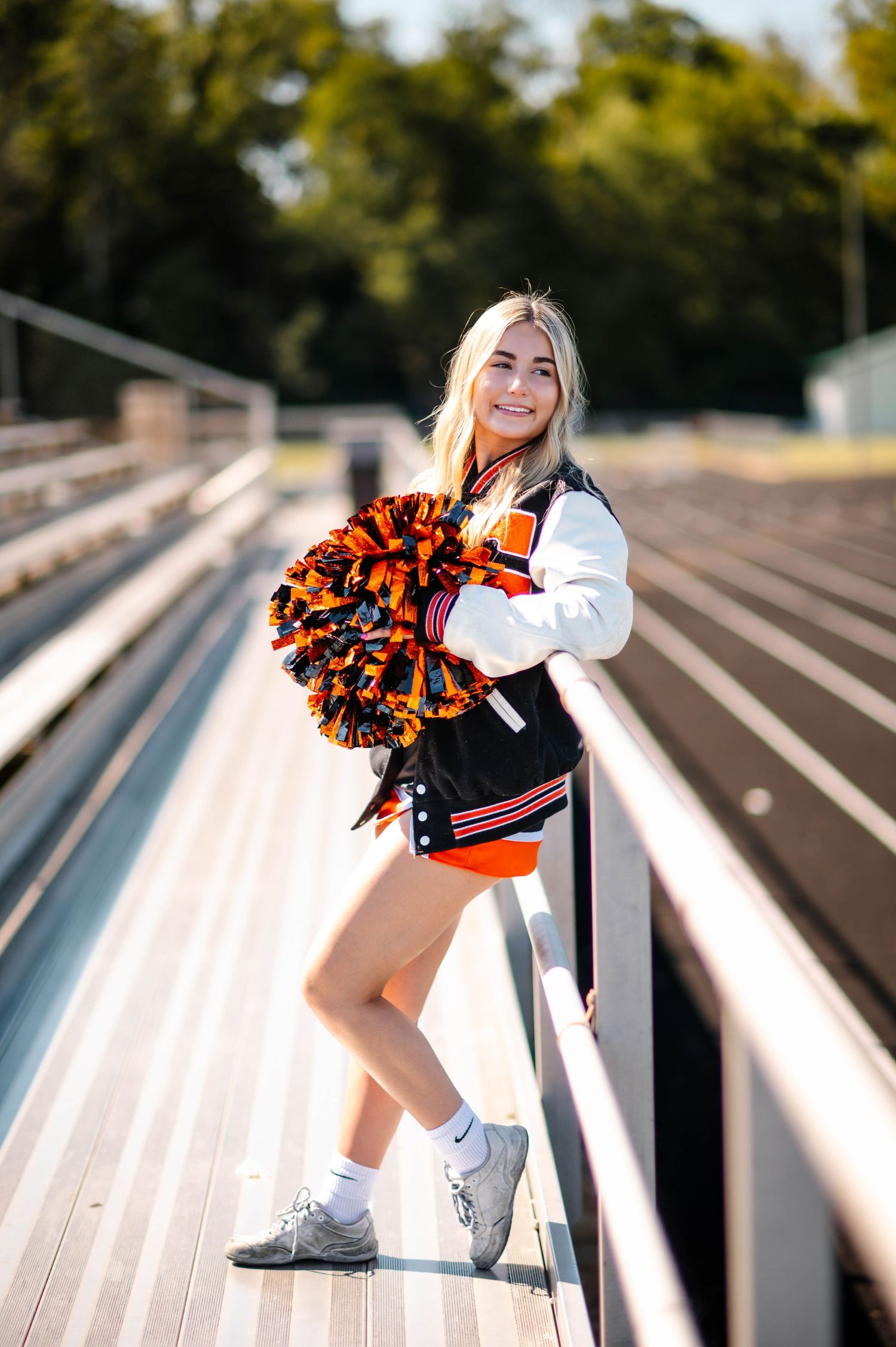 Cheerleader performs dynamic poses with pom poms on stadium bleachers.
